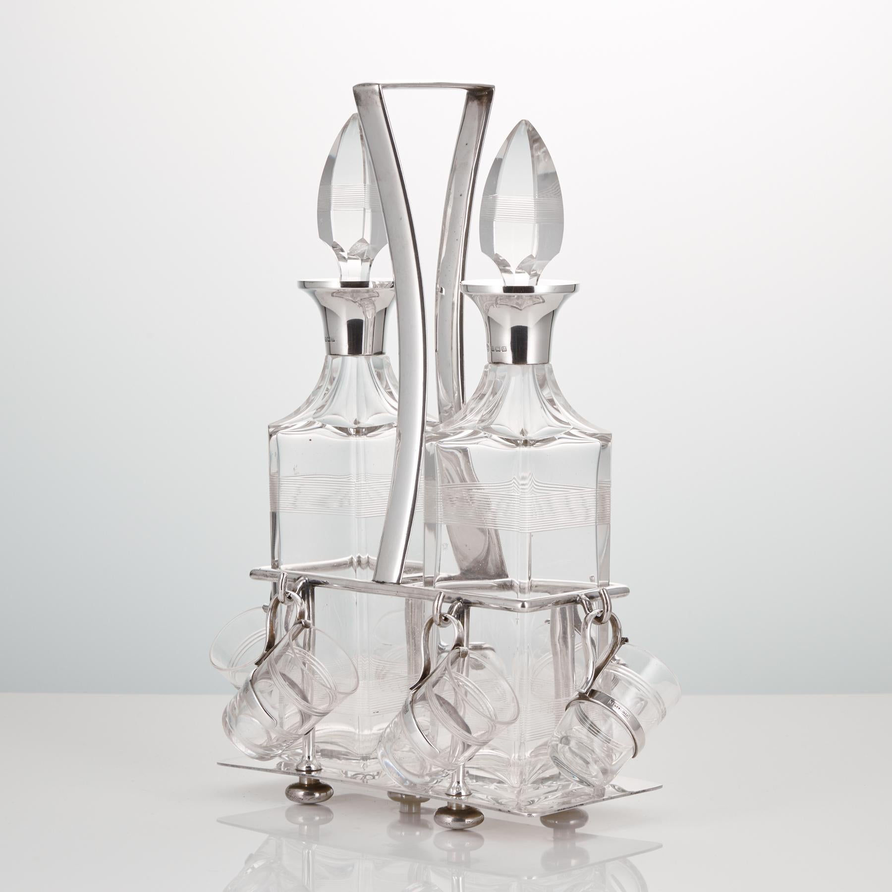 A pair of liqueur decanters with small shot glasses by Hukin and Heath.

The stand is silver plate and marked on the base, the bottle necks and handles for the glasses are sterling silver, hall-marked for Birmingham, 1912.

Hukin and Heath. The