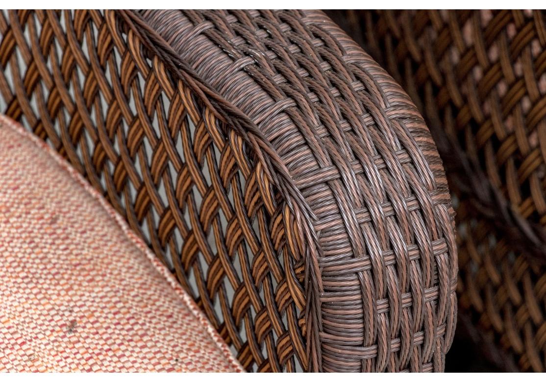 Well constructed comfortable all season armchairs on openwork circular swivel bases. They are woven in vinyl wicker in dark brown for the frames with lighter lattice pattern back, sides and curved skirts. Raised on dark brown swivel bases. Along