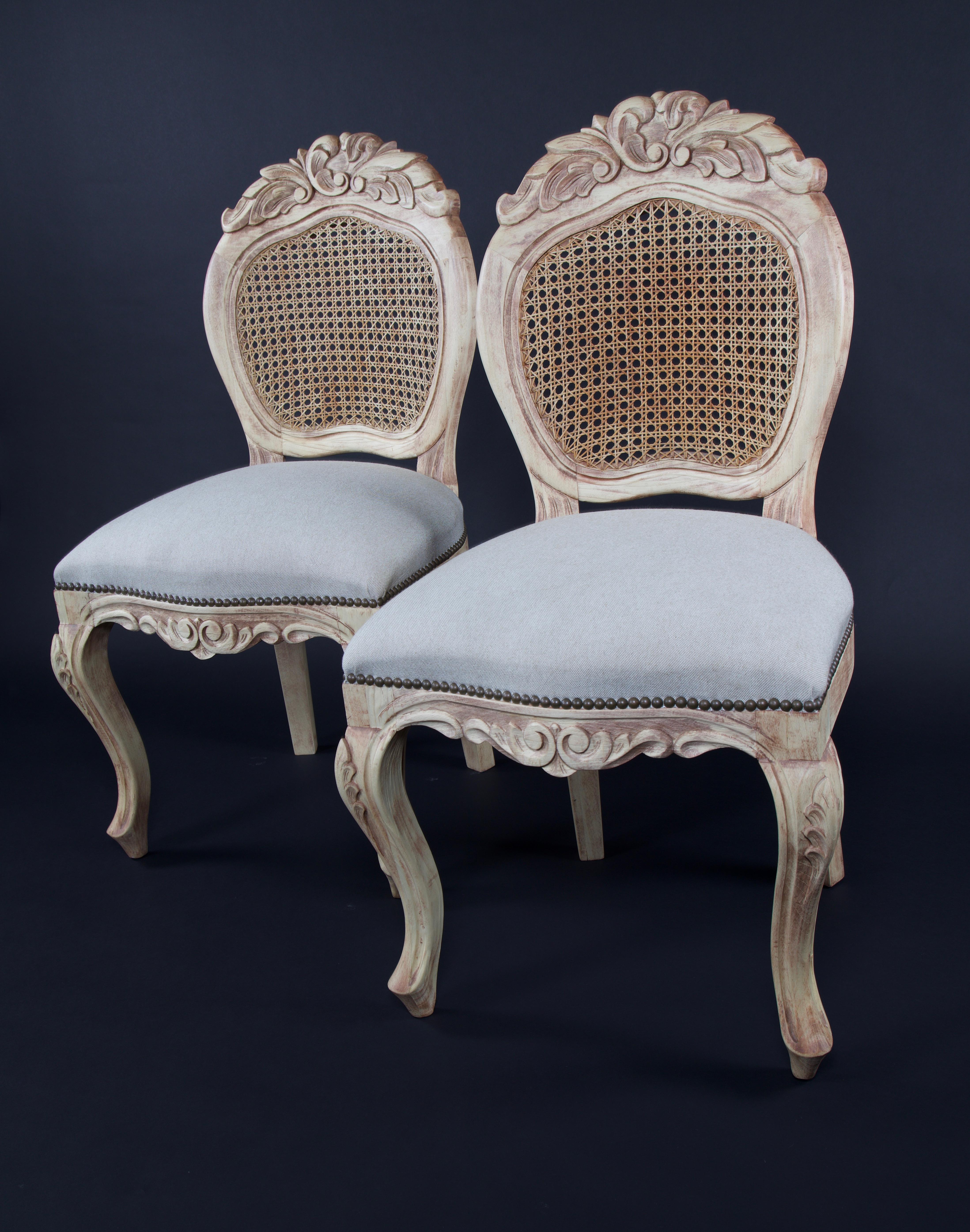 A pair of round side chairs in the style of Louis XV with cabriole legs headed with carved acanthus leaves, a round caned back with cresting that is embellished with multiple carved acanthus leaves with beads and an apron which has a pair of mirror