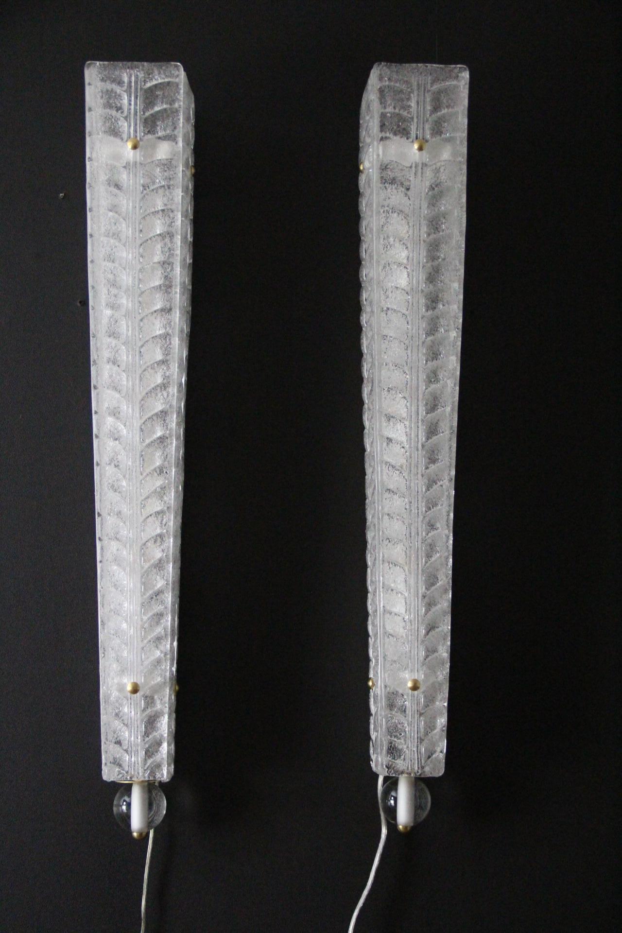 Este exquisito par de apliques de cristal de Murano Graniglia está texturizado con un diseño en forma de hoja, en color blanco. De forma alargada, tres placas de cristal se estrechan en la parte inferior, culminando en una esfera de cristal. Su