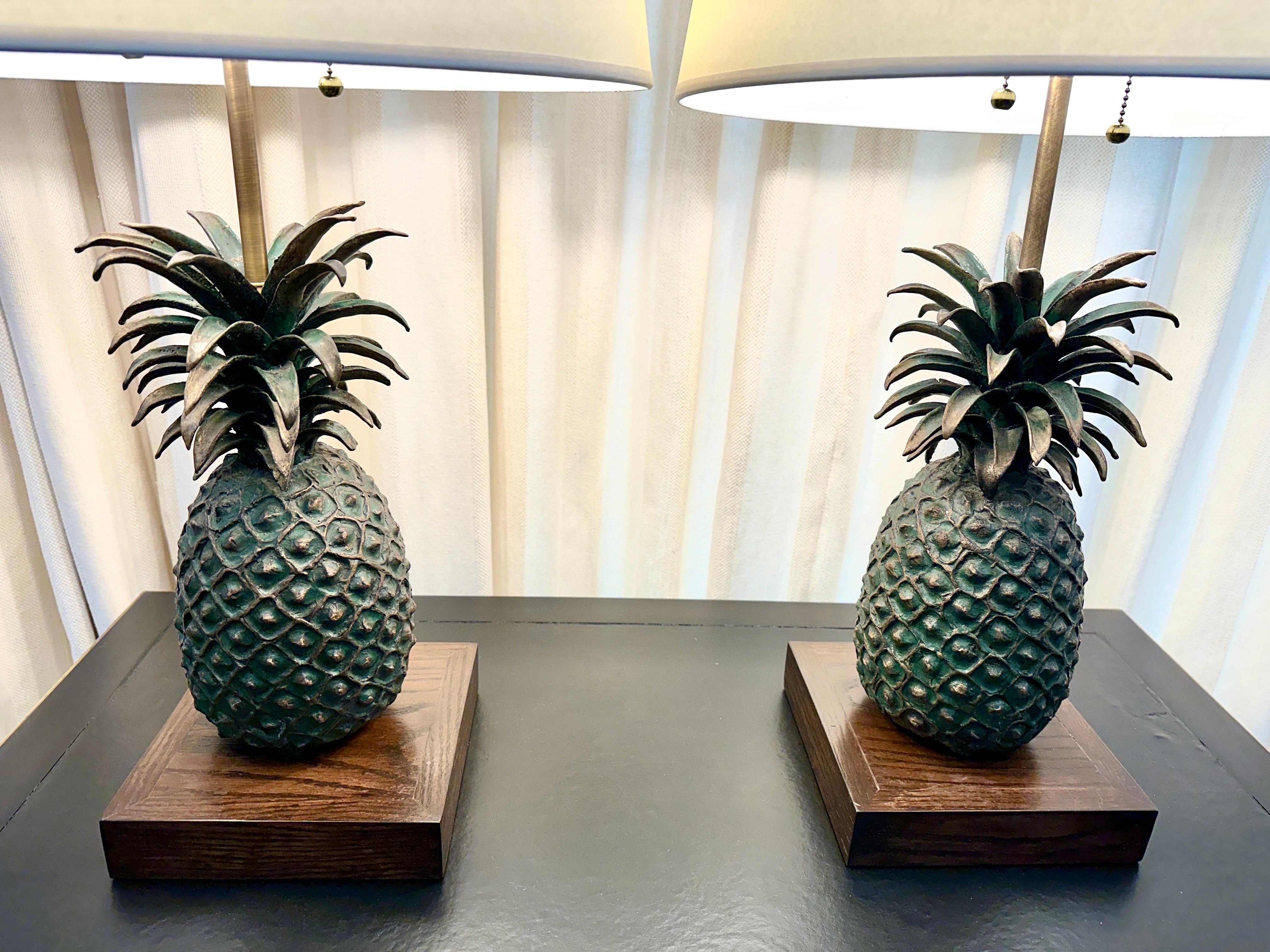 These pineapples were made from the lost wax process in early 20th C. Pineapples are a traditional Western symbol of welcome.  They are heavy solid bronze pineapples mounted on a stained oak wood base, the patina to the bronze has a green hue (see