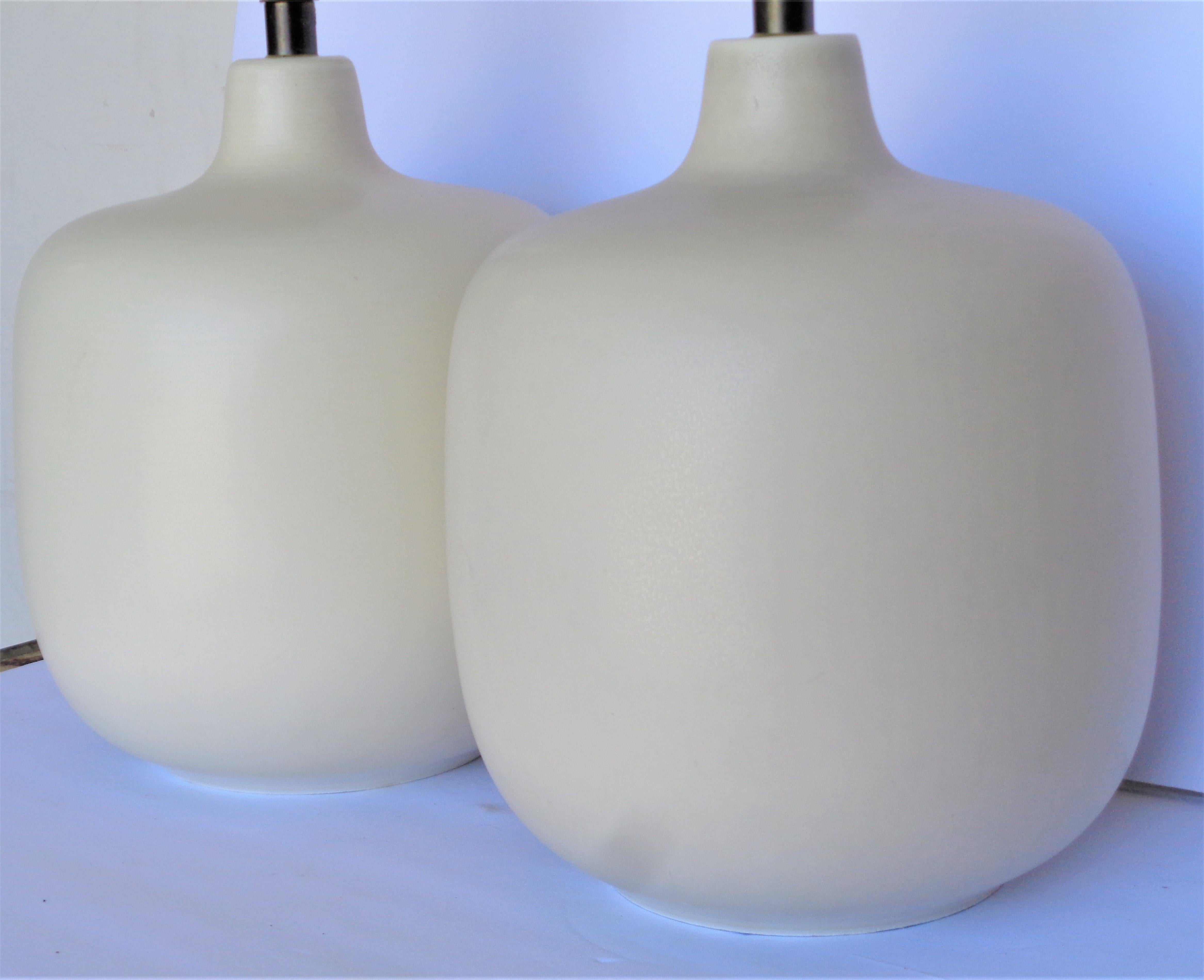 A pair of stoneware table lamps in the original soft eggshell white subtlety textured glaze by Lotte and Gunnar Bostlund, Denmark. Lamps measure 13 inches high to top of ceramic, 16 inches high to top of electric socket, 10 inches wide, 10 inches