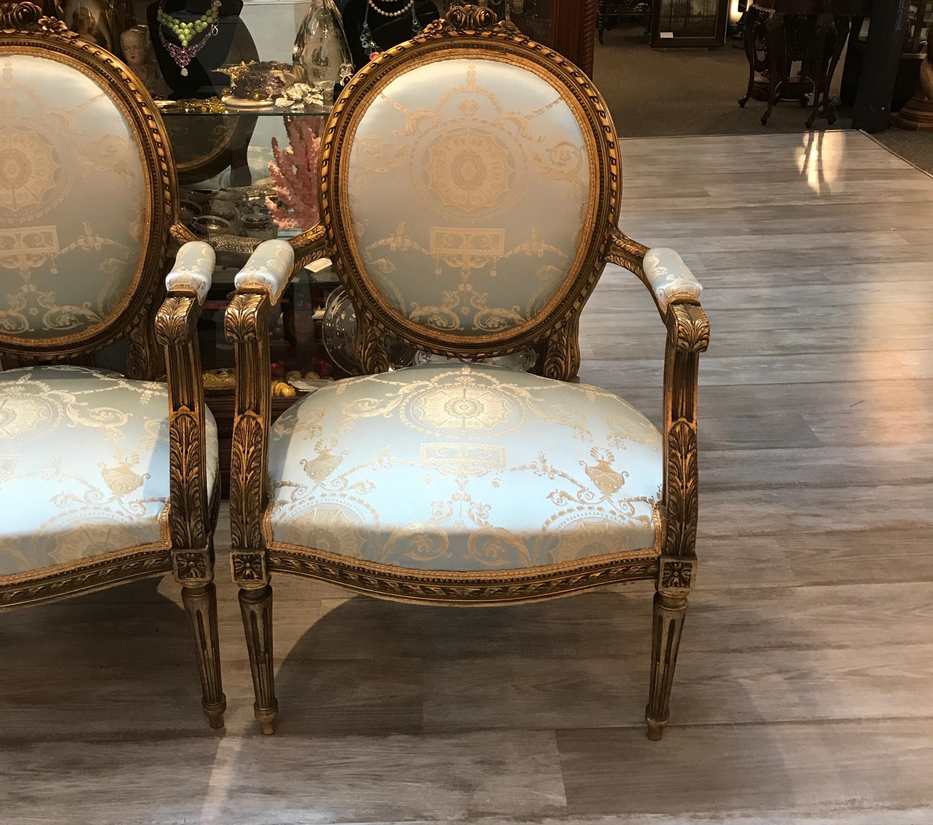 Of typical form, the oval back with bowed top and beautiful carved open arms. Bound reed motif on frame with acanthus leaf appointments. The chair rests on Classic reeded tapered legs. These chairs are newly recovered in an elegant Marie Antoinette