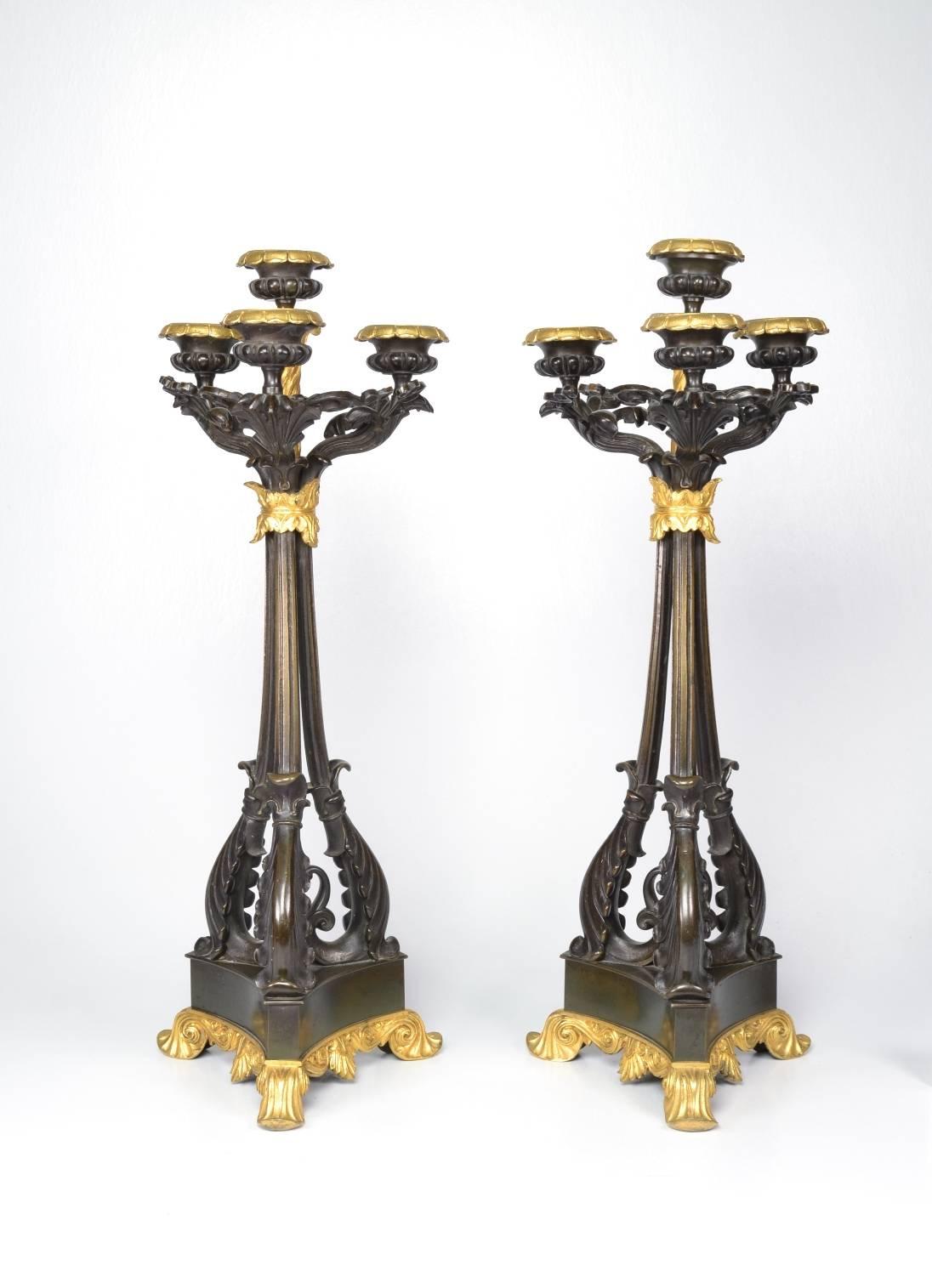 Pair of bronze and ormolu (bronze doré) four-light candlesticks, each with gold floral bobeches and leafy arms raised on three scrolling branches bundled at the top; the triangular base raised on doré feet.

These unusual candelabra are well cast