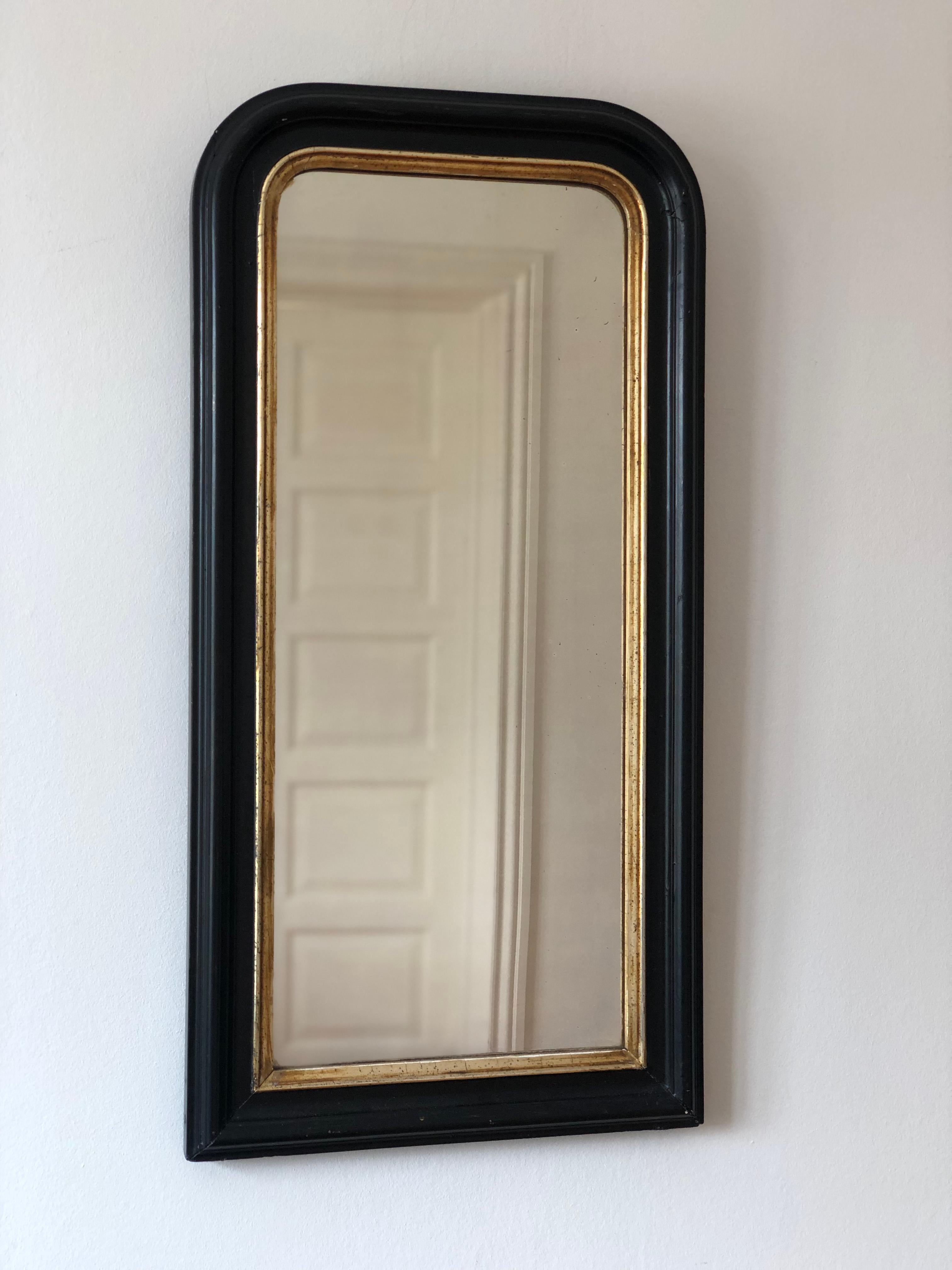 An enchanting pair of original Louis Philippe mirrors from France, dating to the late 19th century. Each small full-length mirror features a refined black frame with soft gilt trim, mercury glass, and a gracefully curved top, exuding timeless