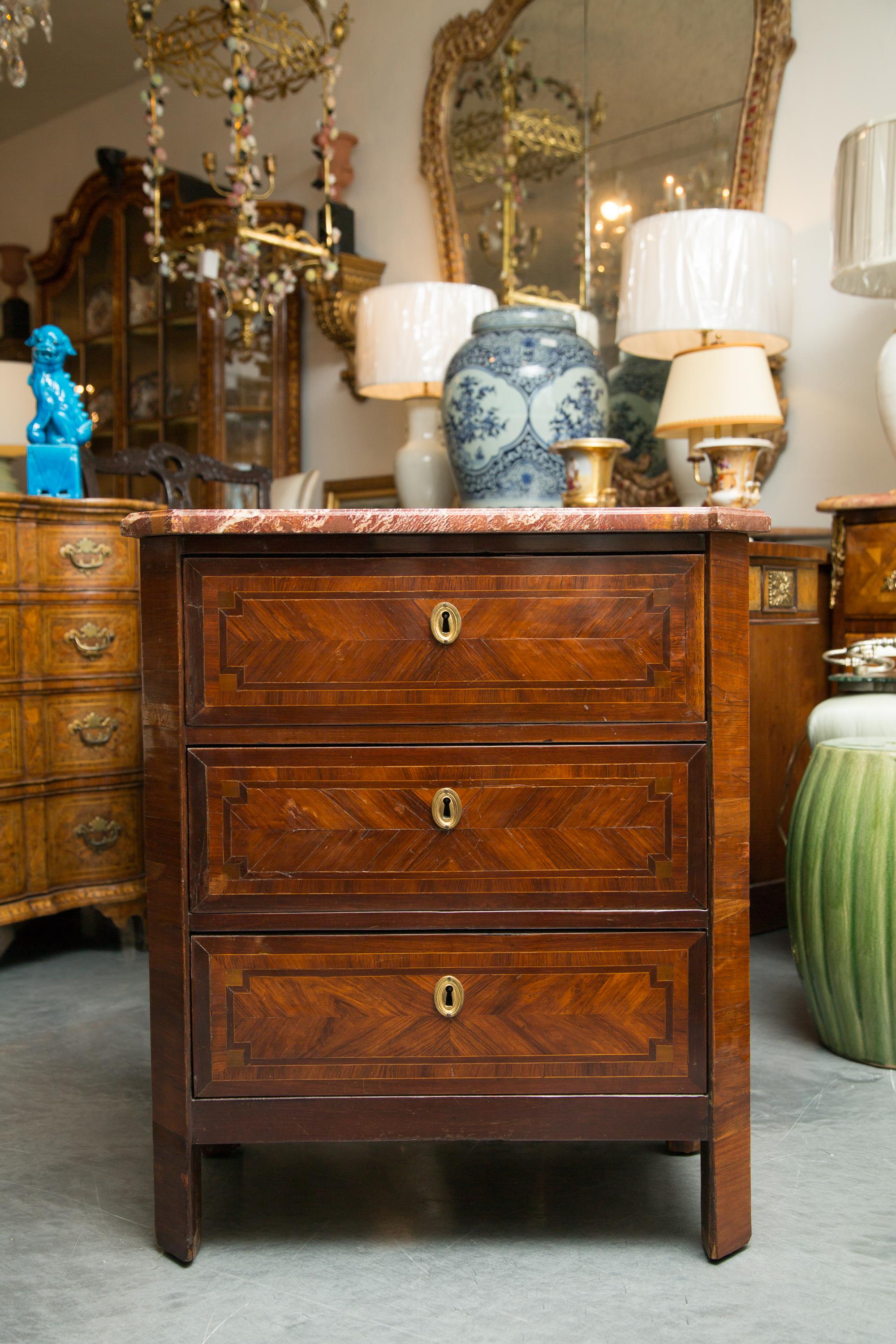 This is a charming pair of Louis Philippe commodes. There is a variegated rouge marble top over a bank of three drawers with chevron veneer faces, raised on straight canted feet, circa 1840.