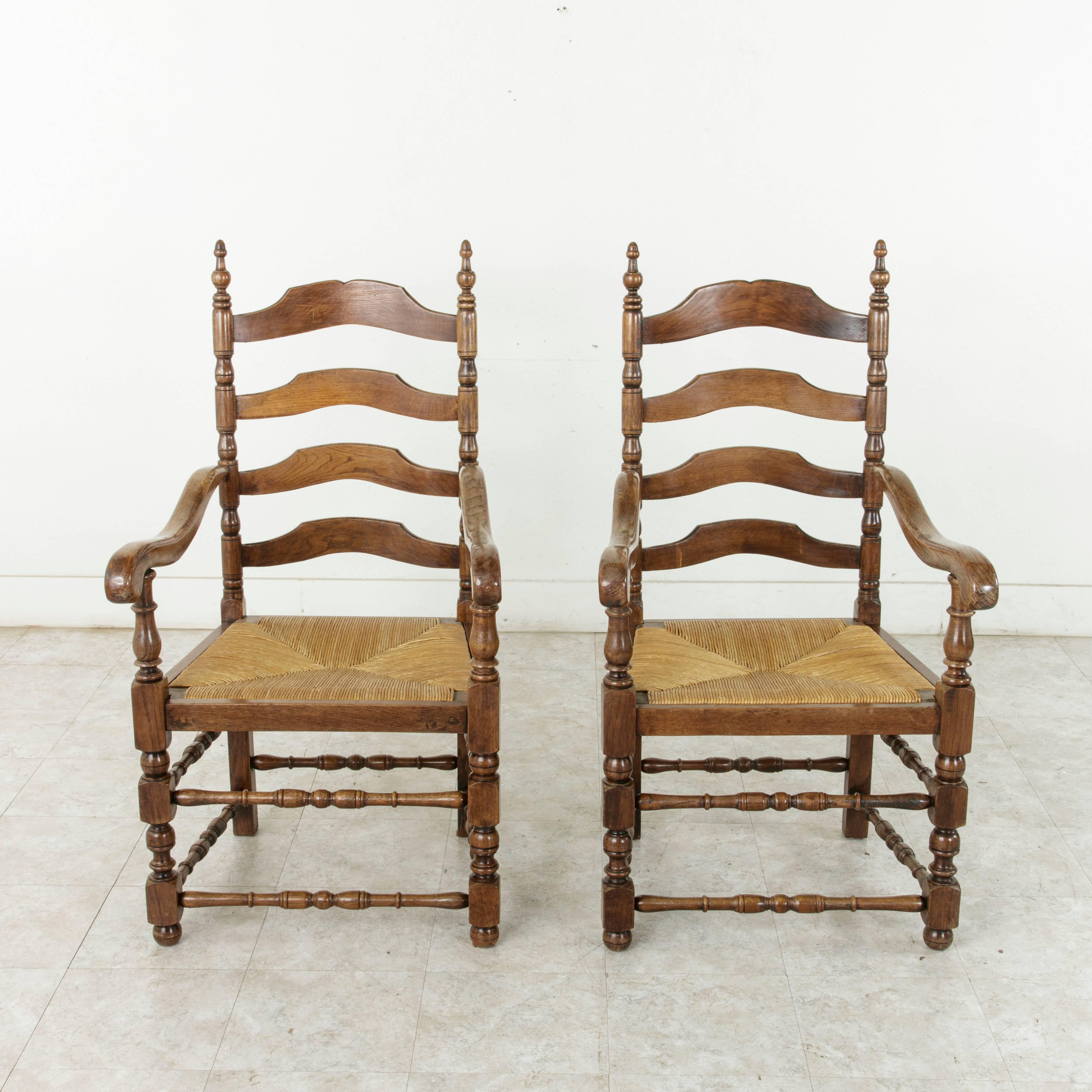 This pair of Louis Philippe style oak ladder back armchairs features turned legs and rush seats. Multiple turned crossbars between the legs provide extra stability. The unusually large rush seats measure 20 inches wide and 19 inches deep, and are
