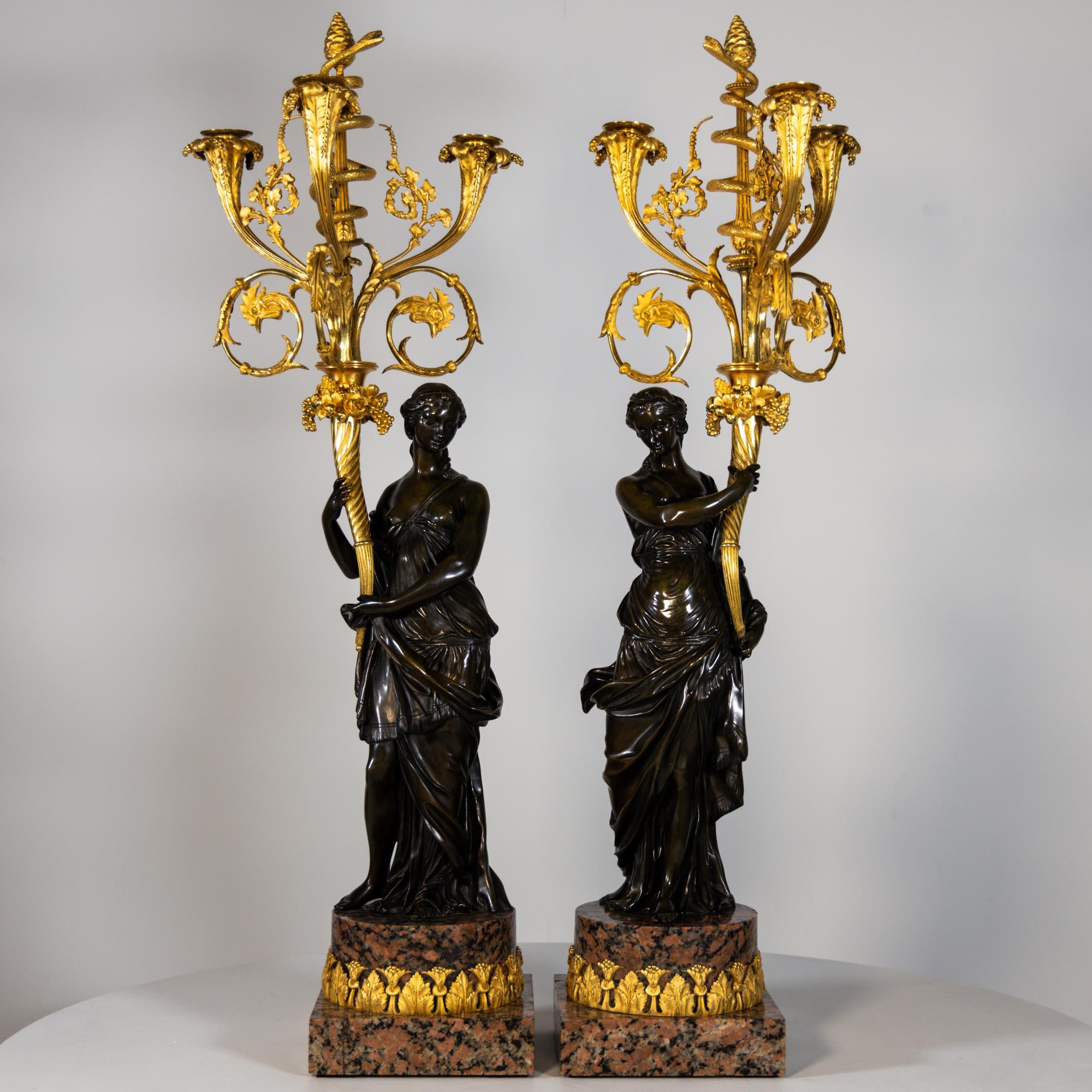 Pair of candelabra made of fire-gilt and burnished bronze. The female figures are depicted in ancient dress and carry cornucopias that develop into projecting candelabra and end in a spiralling serpent around the central thyrsos staff with pine