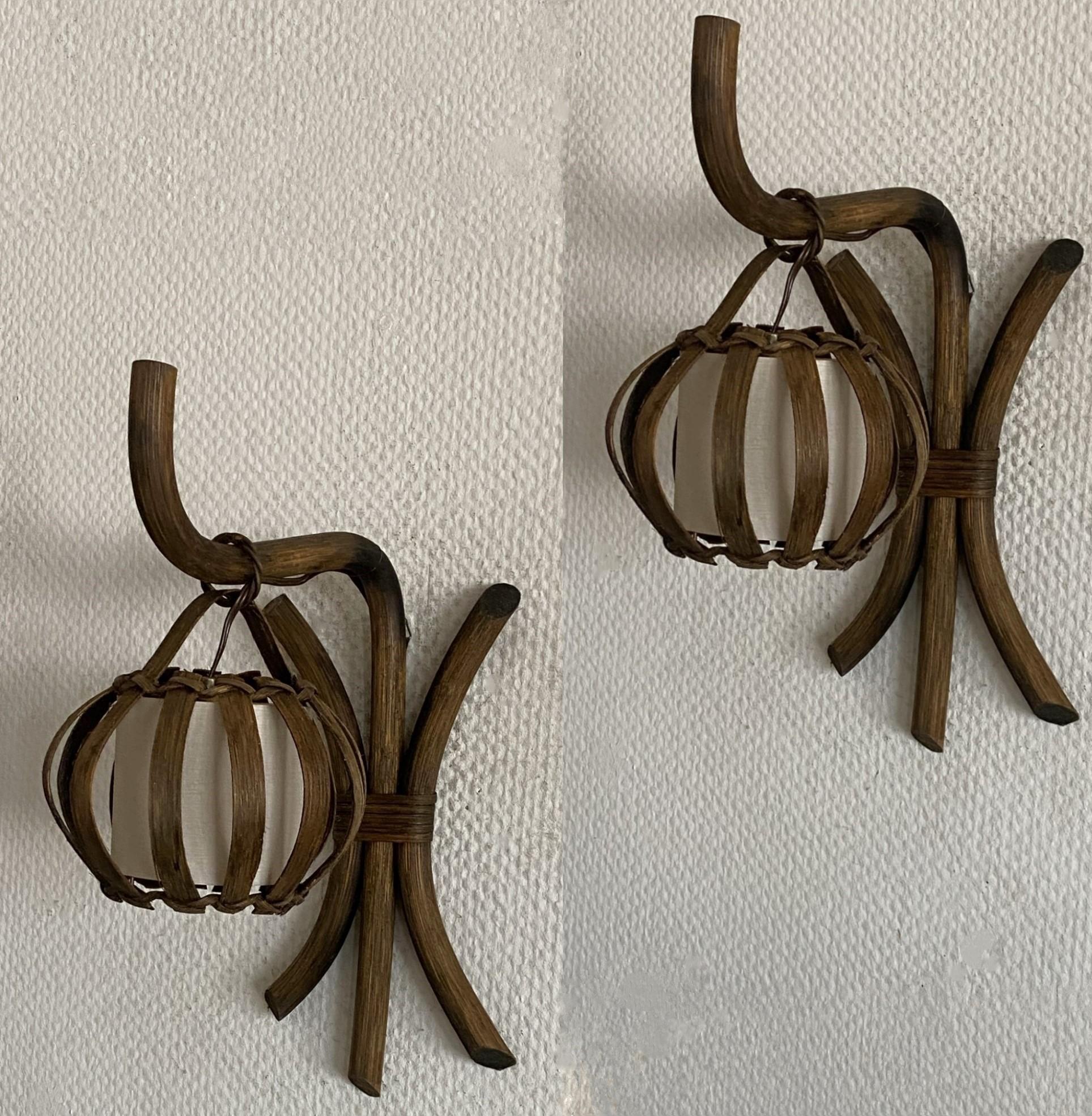 A pair of lovely  bamboo and rattan wall sconces by Louis Sognot, France, 1960s. Bamboo wall mounted backpiece with hanging lantern shape rattan lamp shades, with fabric shades inside providing a warm and pleasant lighting. These wall conces are