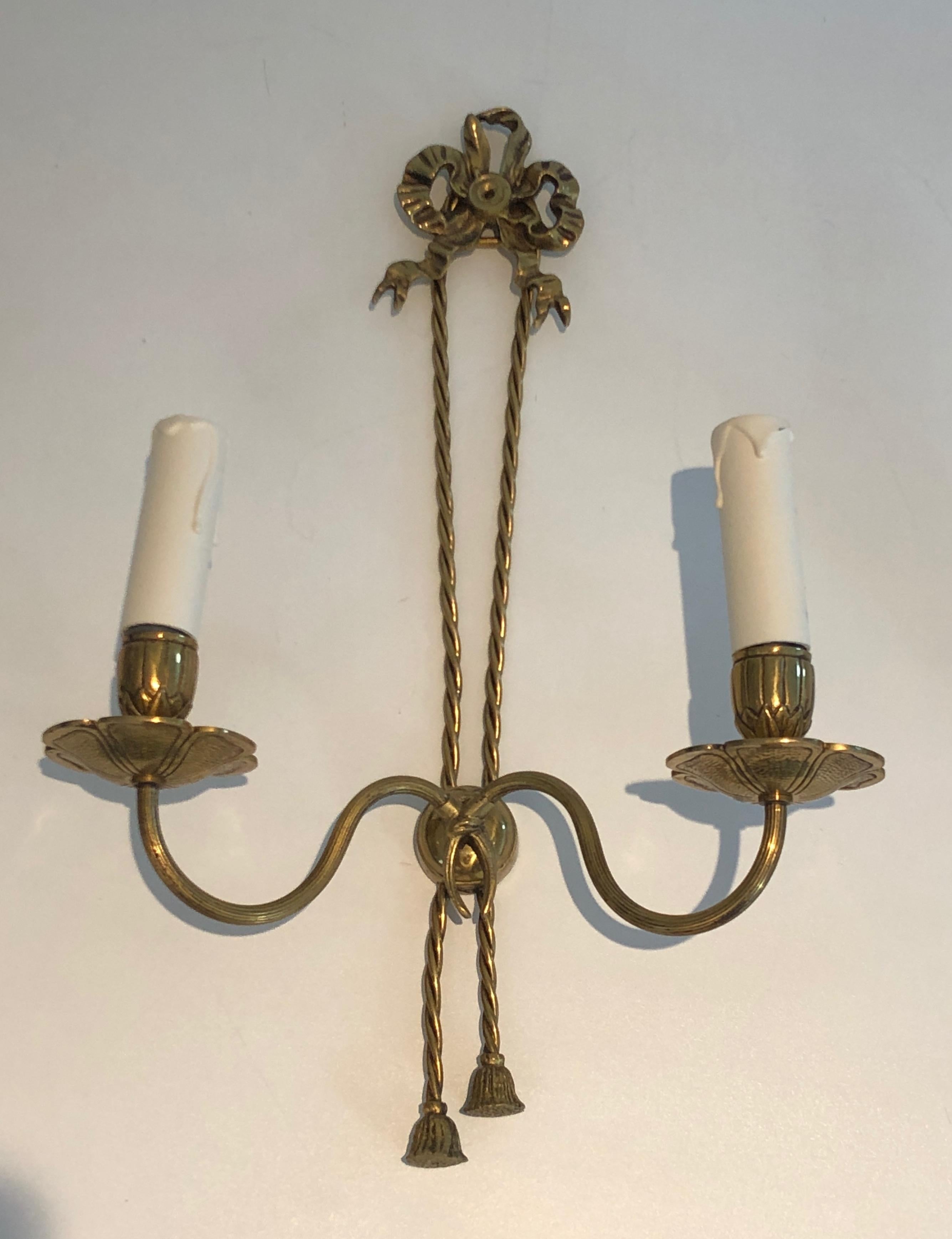 This pair of Louis the 16th style wall sconces is made of bronze. These wall lights are very decorative, they have a large noddle on top with twisted ribbons going from top to bottom. This is a French work, circa 1950.