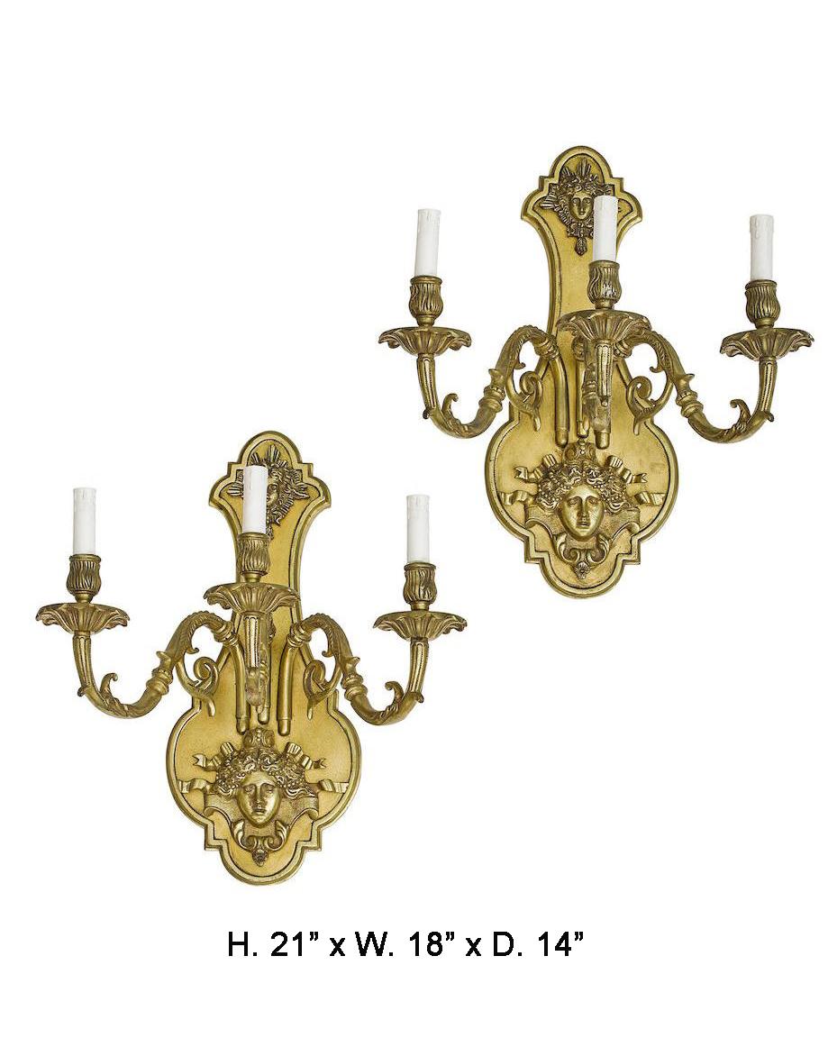 Pair of large Louis XVI style bronze two light sconces.
A shaped gilt bronze backplate decorated with two female masks within foliate and ribbons, issuing three foliate-inspired candle arms, terminating in dishpan and candle holder.
Electrified.