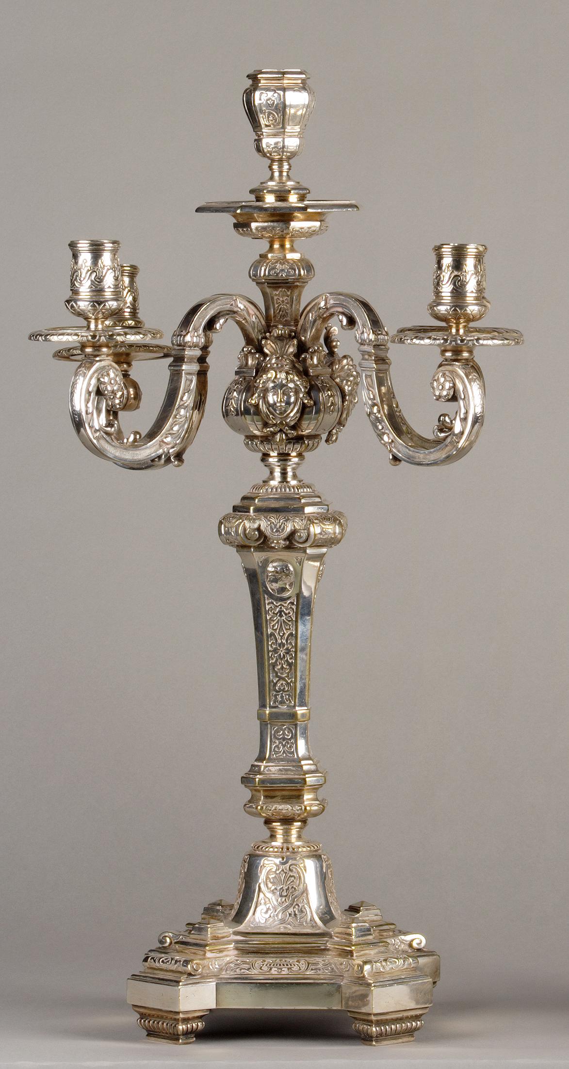 Pair of Louis XIV style five-light candelabras. Chiseled and silvered bronze. Ornamented with palmettes, medallions and feminine masks. Central stem with guilloche motifs, resting on an octagonal base.

To be linked: a silver candlestick made