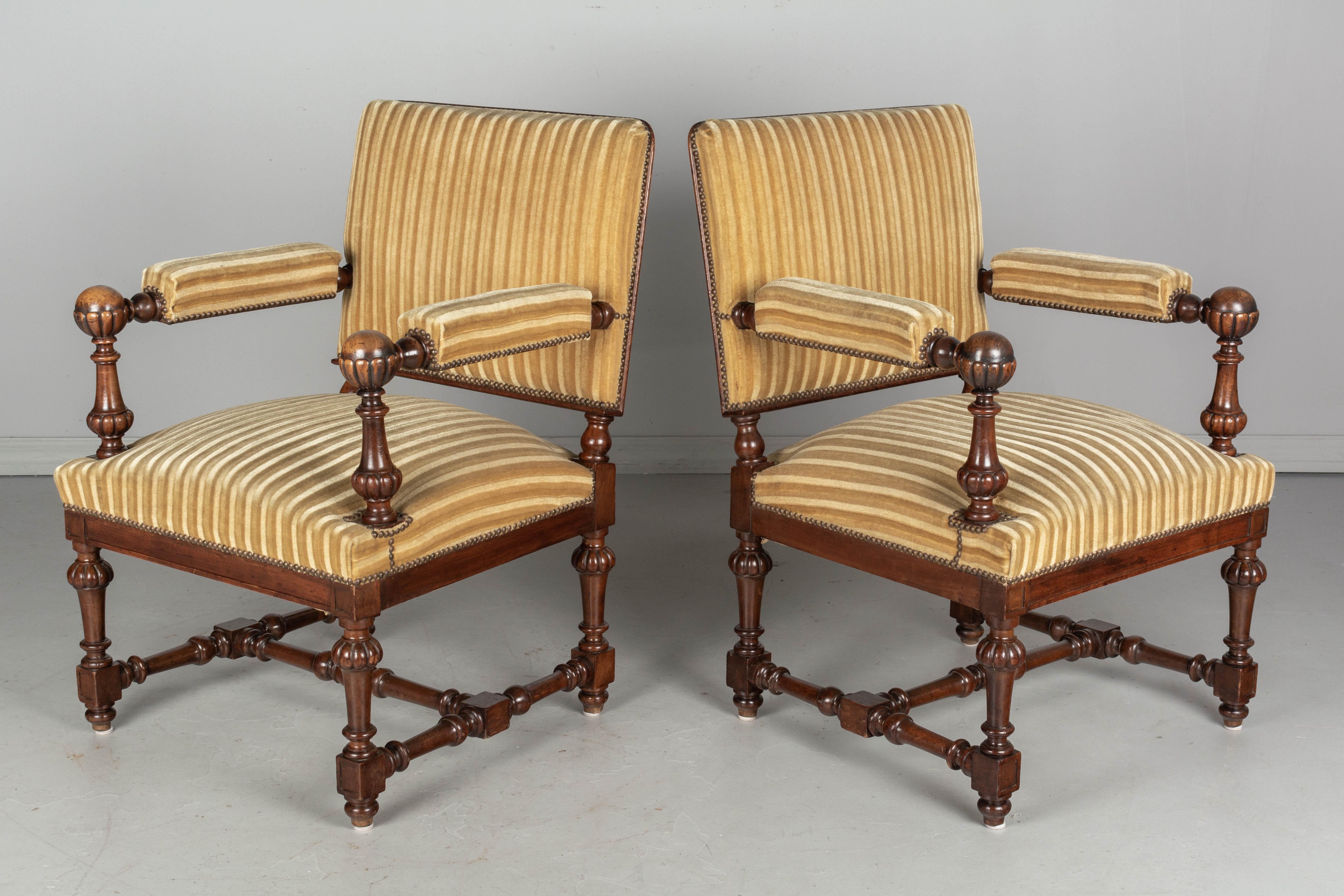 A pair of Louis XIV style French fauteuils, or arm chairs, with solid walnut frames. Boldly carved armrests with large ball finials and turned wood spindle legs and stretcher. Nice proportions with square profile, sturdy construction and comfortable