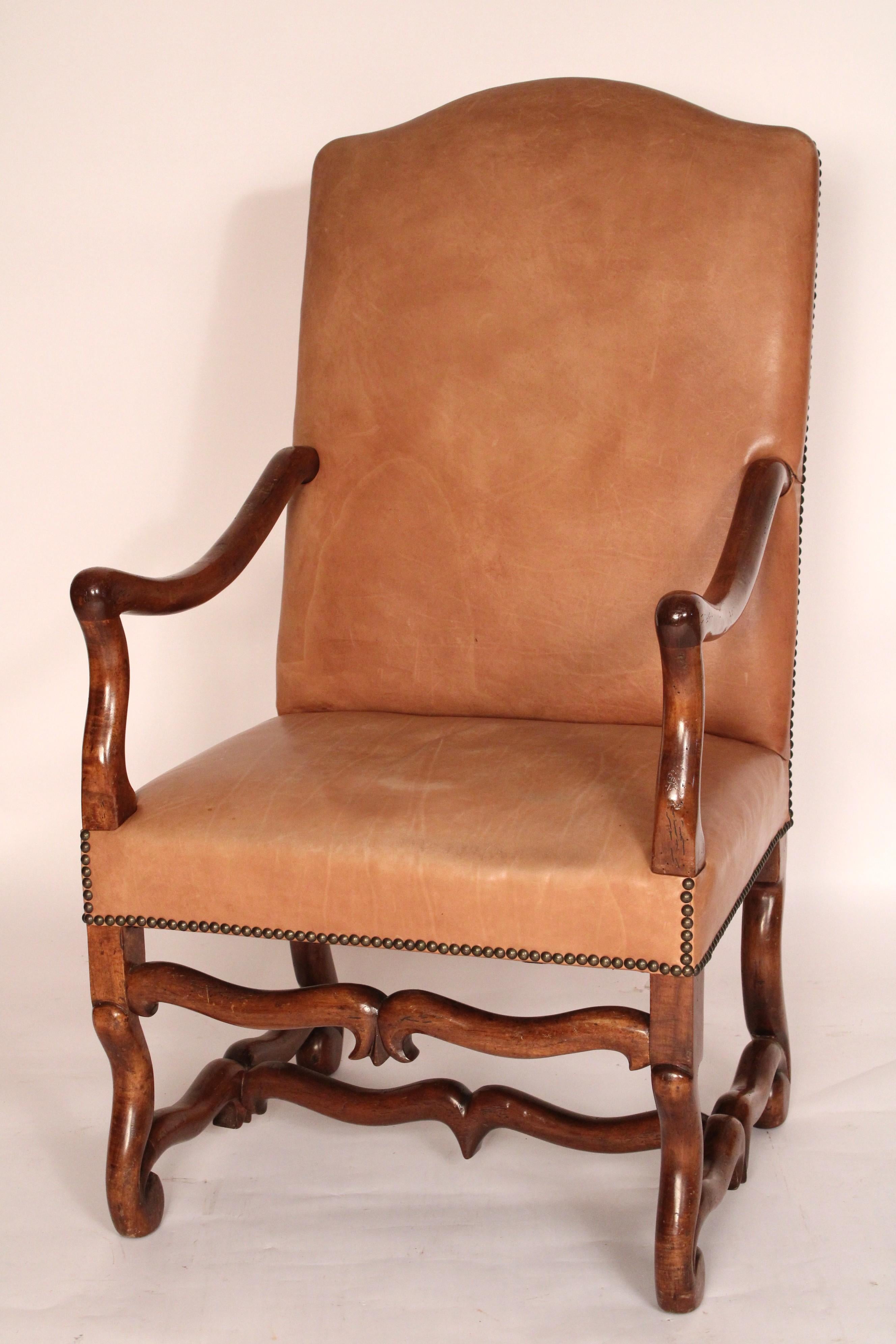 Pair of Louis XIV style leather upholstered walnut armchairs, circa 1950's. With a cupid's bow crest rail, upholstered leather backs and seats with brass nail heads, down swept arms, serpentine shaped arm supports, os de mouton legs joined by