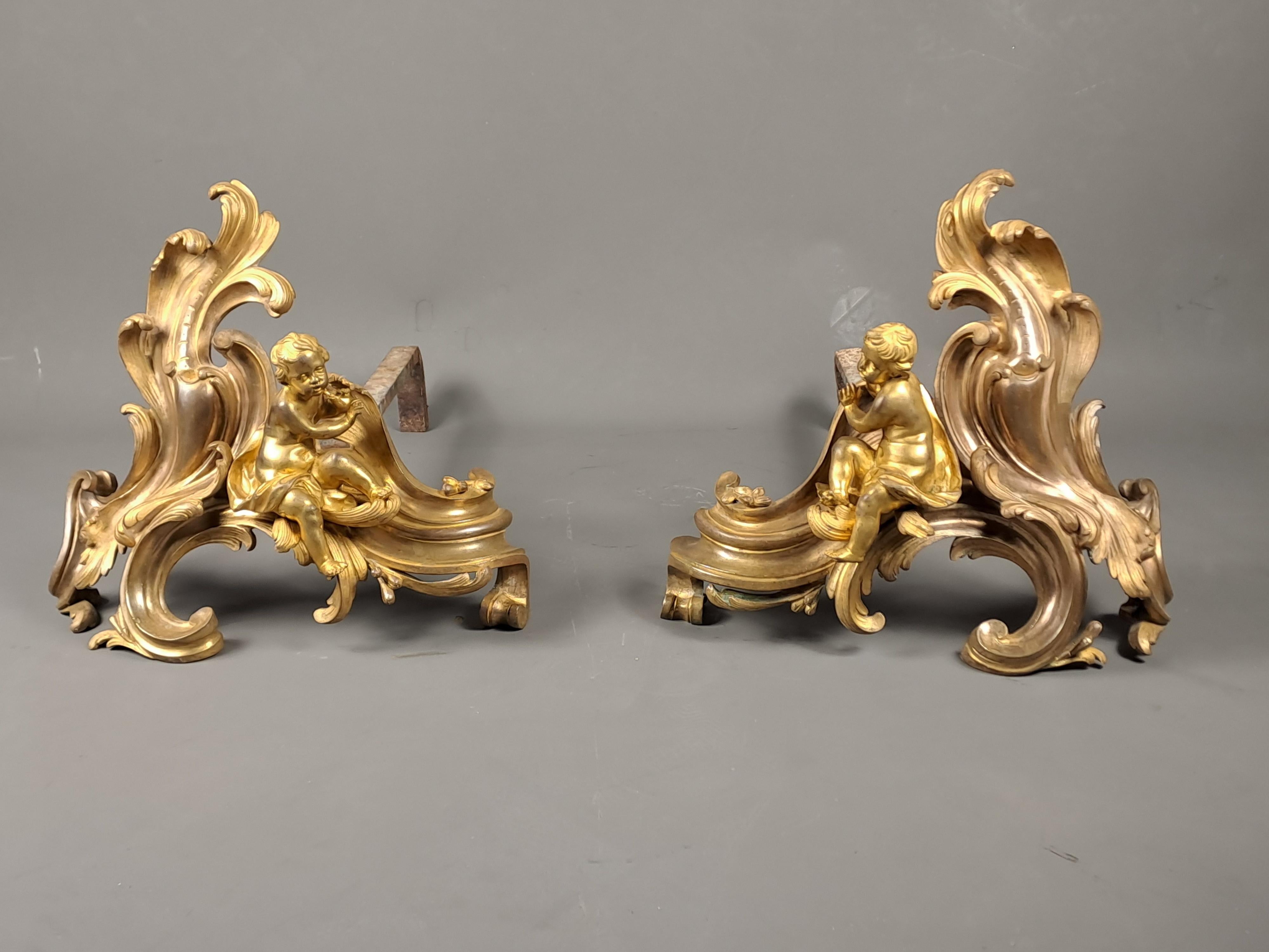 Pair of Louis XV andirons in finely chiseled gilded bronze decorated with chubby putti warming their hands, seated on a rococo decoration.

French work from the 18th century of good quality.

In good condition but wear to the gilding