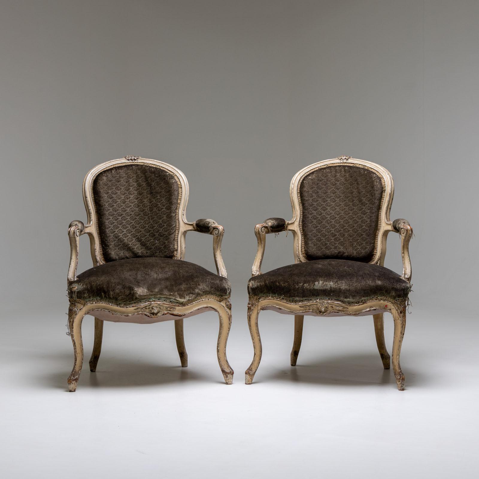 Pair of armchairs with curved frames and S-shaped legs. The seat, backrest and armrests are upholstered. The armchairs have a white patina and are in used condition.