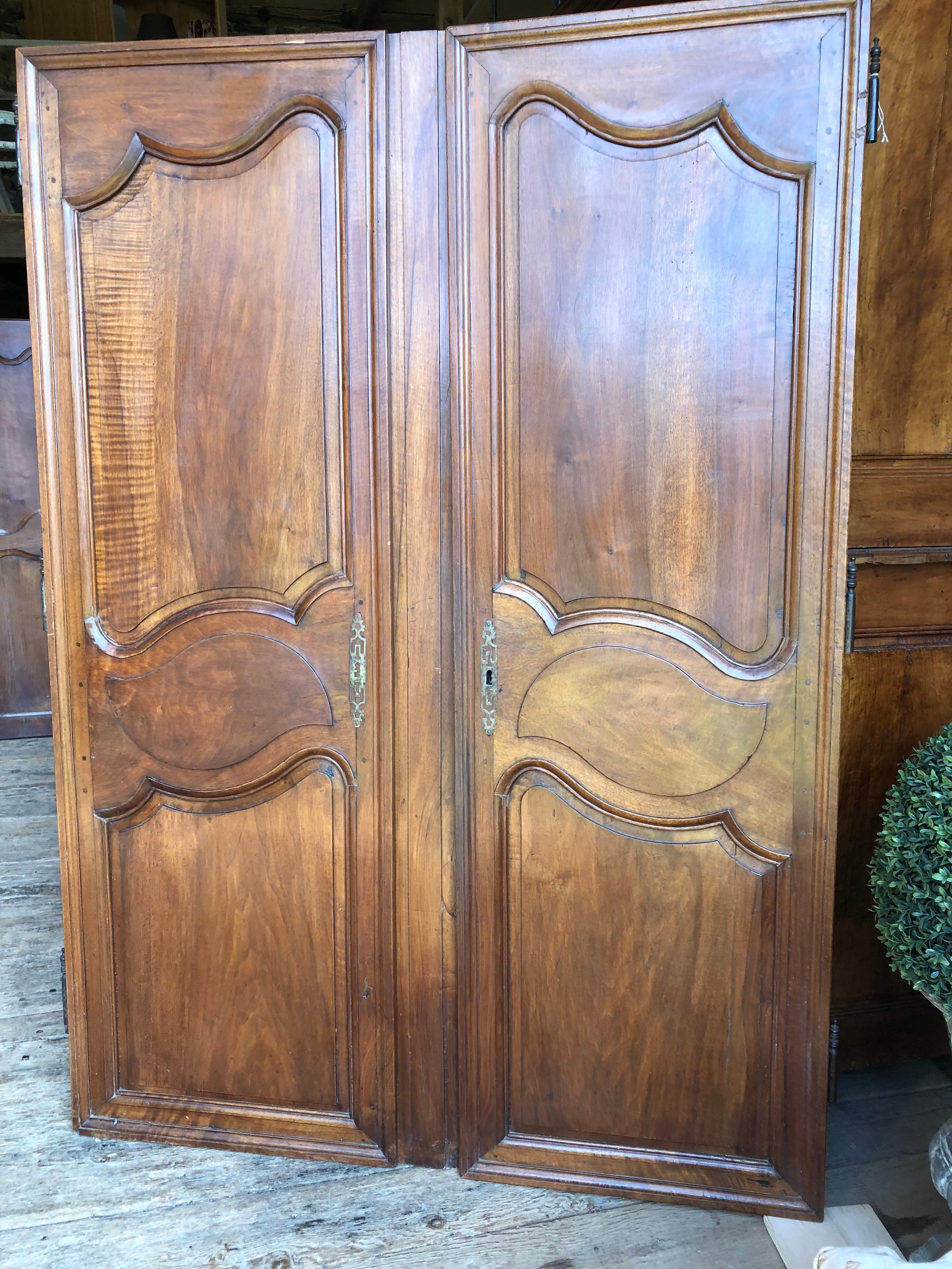 A nice pair of tall Louis XV period walnut armoire doors, circa 1760, nicely paneled and retaining their original iron hardware. 
The center panel which is attached to the left side door can be removed to create a pair of doors the same size with