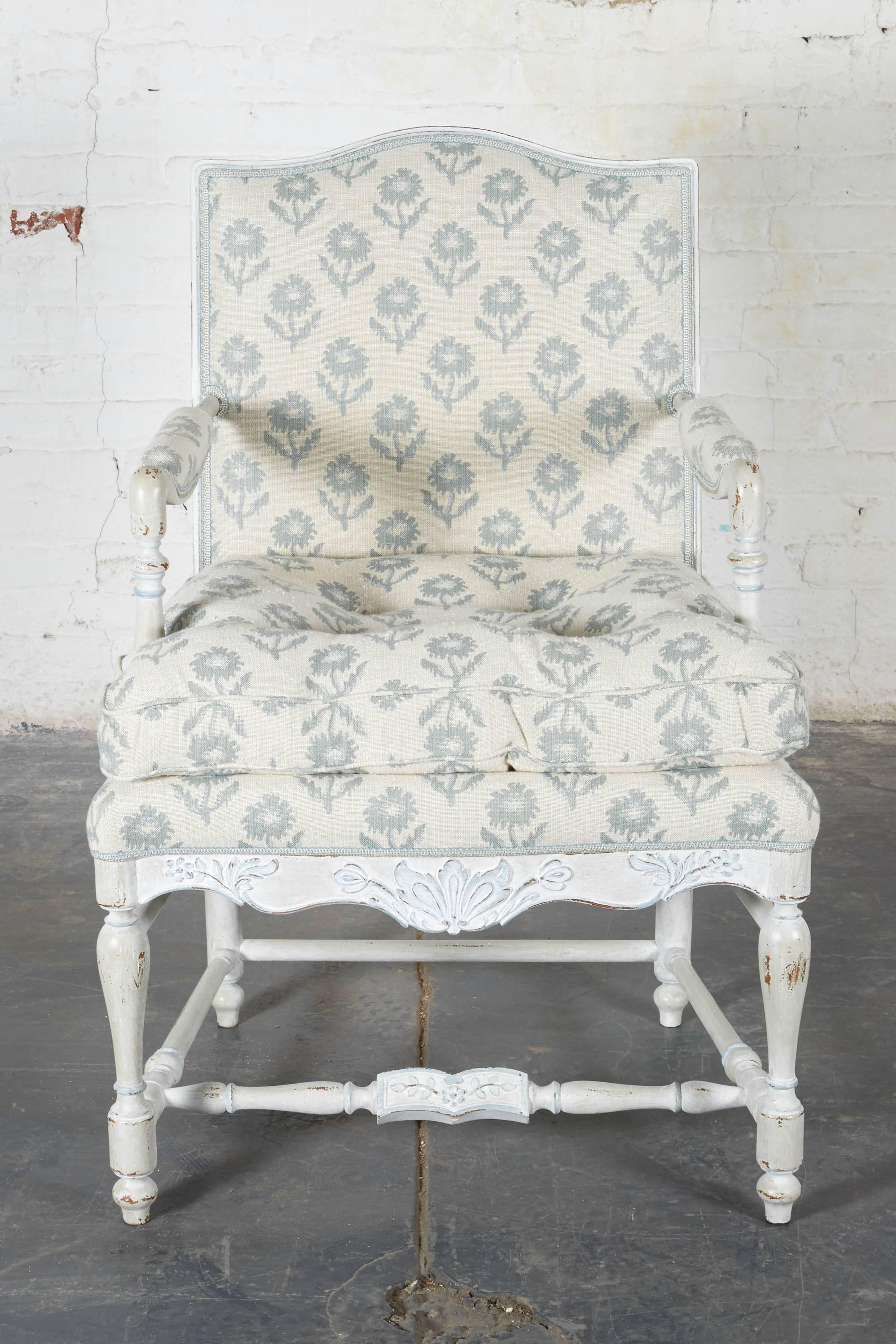The upholstered back with arched crest rail and issuing padded armrests; the seat with loose cushion over a shaped seat rail carved with foliate sprays picked out in blue; raised on turned legs joined by stretchers.