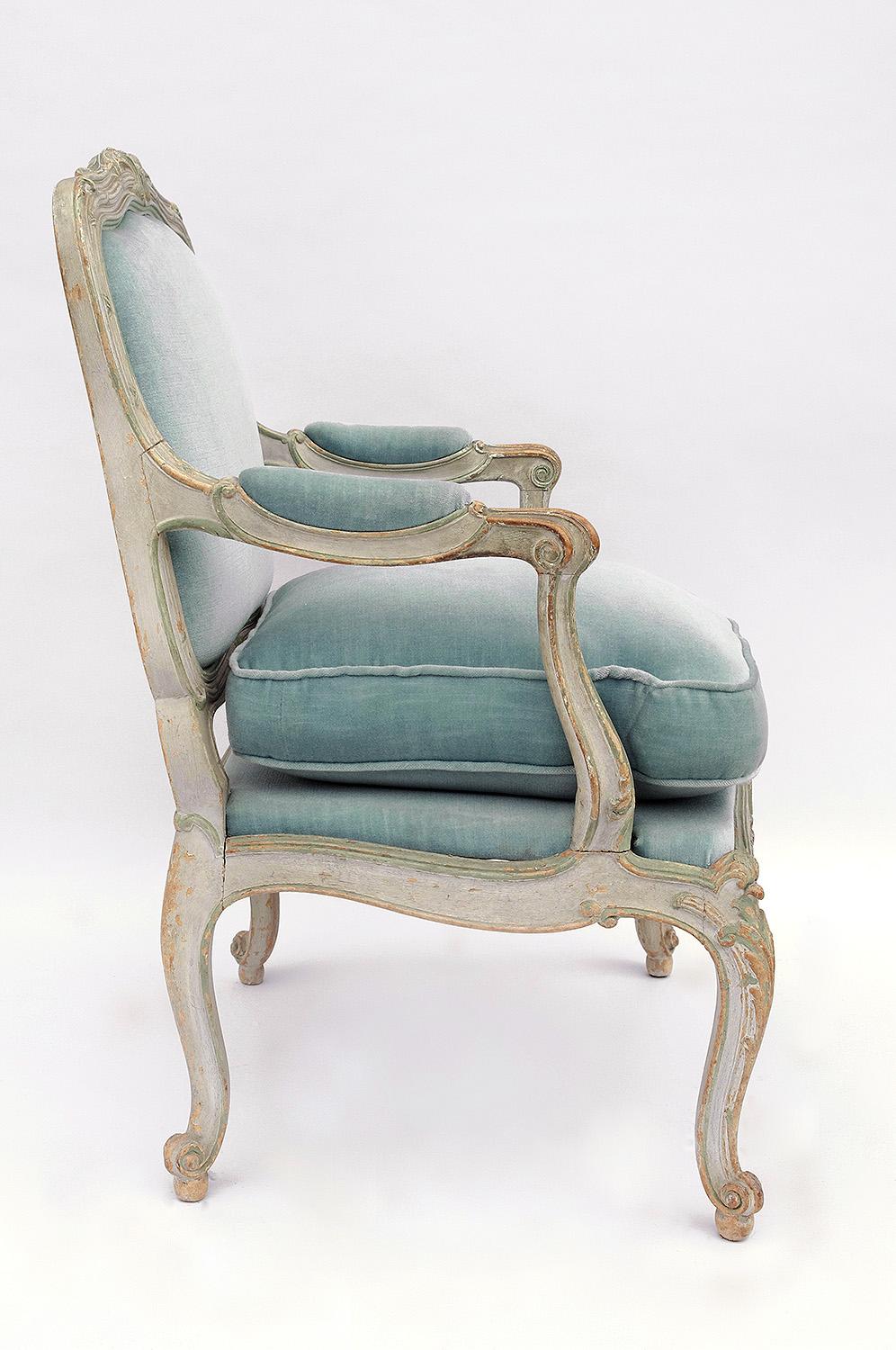 Pair of small Louis XV style armchairs à chassis in carved cream lacquered wood, nice patina. Standing on four console legs ending in swirls. Scalloped trails, armrest support slightly beneath the legs line. A la reine flat serpentine shaped