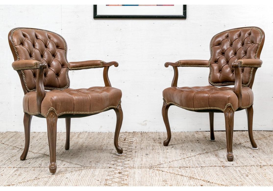 Pareja de fauteuils de cuero marrón de estilo Luis XV, con armazón tallado, manchetas de cuerpo entero y asiento y respaldo acolchados con botones. Las sillas tienen patas cabriolé y motivos de hojas talladas en las rodillas delanteras. 
