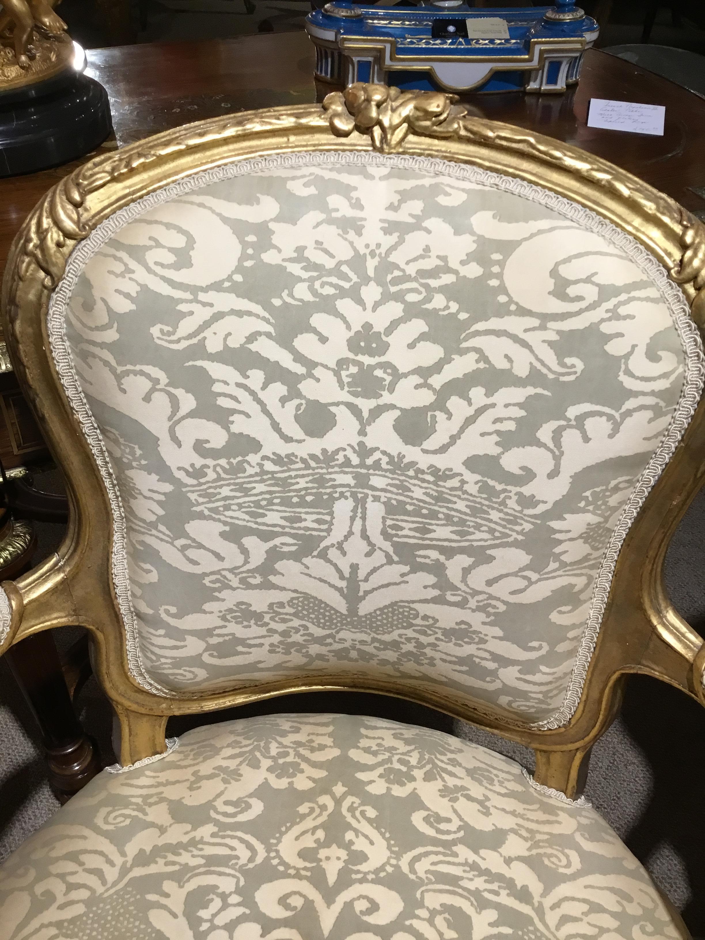 A pair of Louis XV style chairs, 20th century. Upholstered in a cream hue Fortuny fabric.
Carved giltwood with floral motif at center crest.