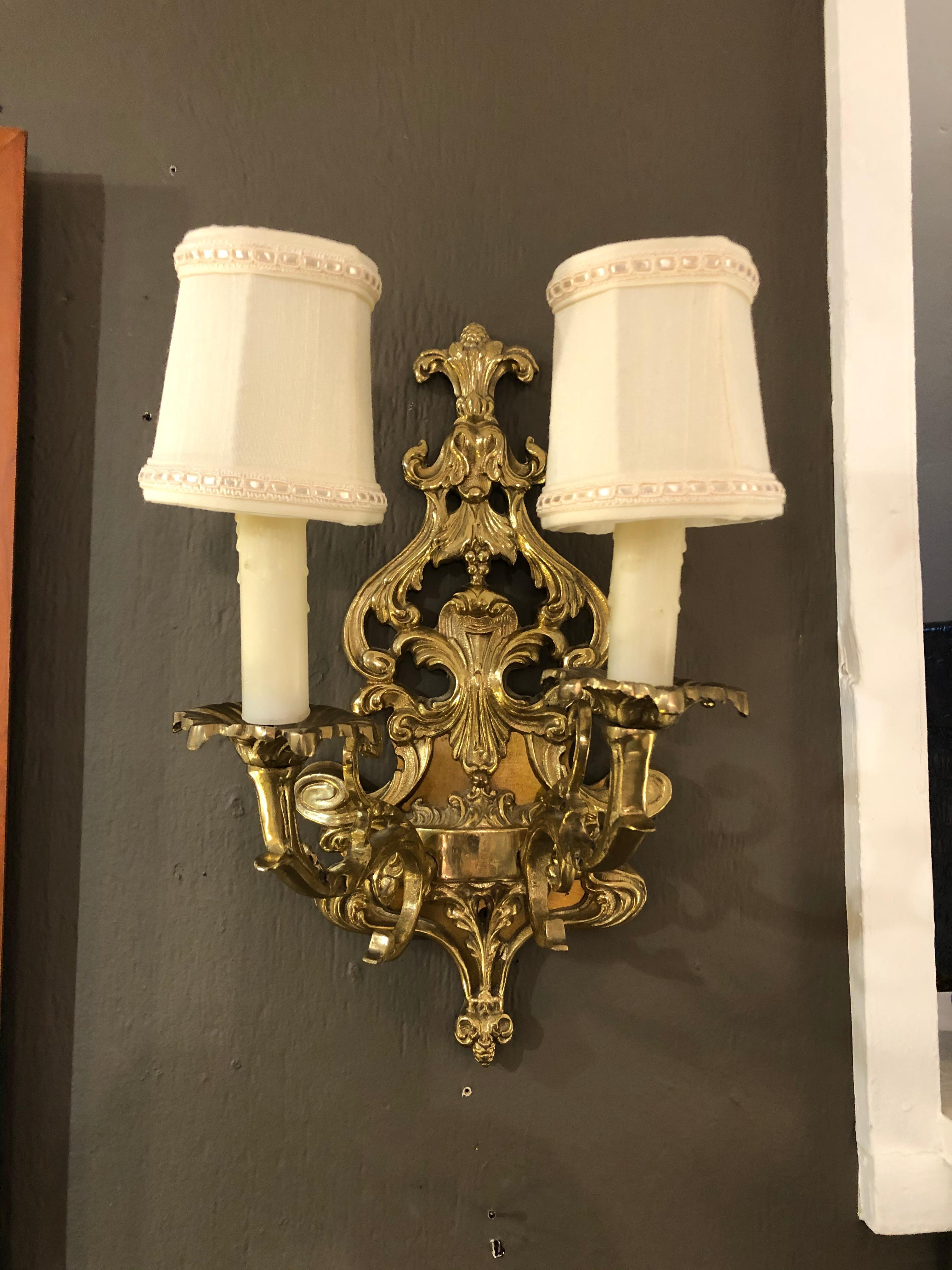 A handsome pair of antique Louis XV style cast bronze wall sconces having two arms each with pierced scroll and foliate serpentine central cartouche in high relief with Fleur di Lis motife.