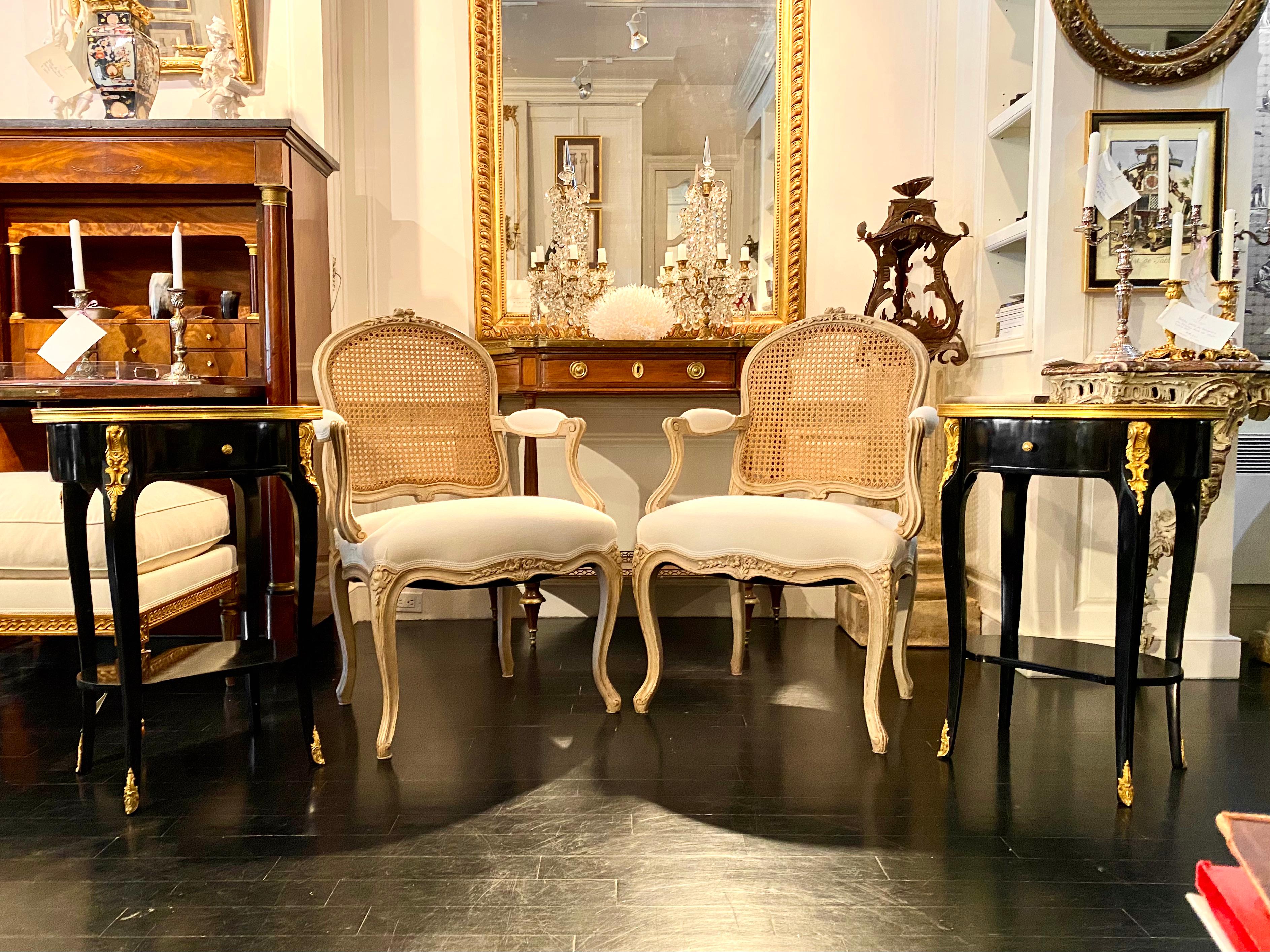 Pair of Louis XV style oval ebonized side tables with marble tops and Ormulu mounts, in the glamorous style of Hollywood Regency. This two-tiered, pair of black lacquer tables is composed of ebonized wood with gilt bronze mounts. The pair of tables