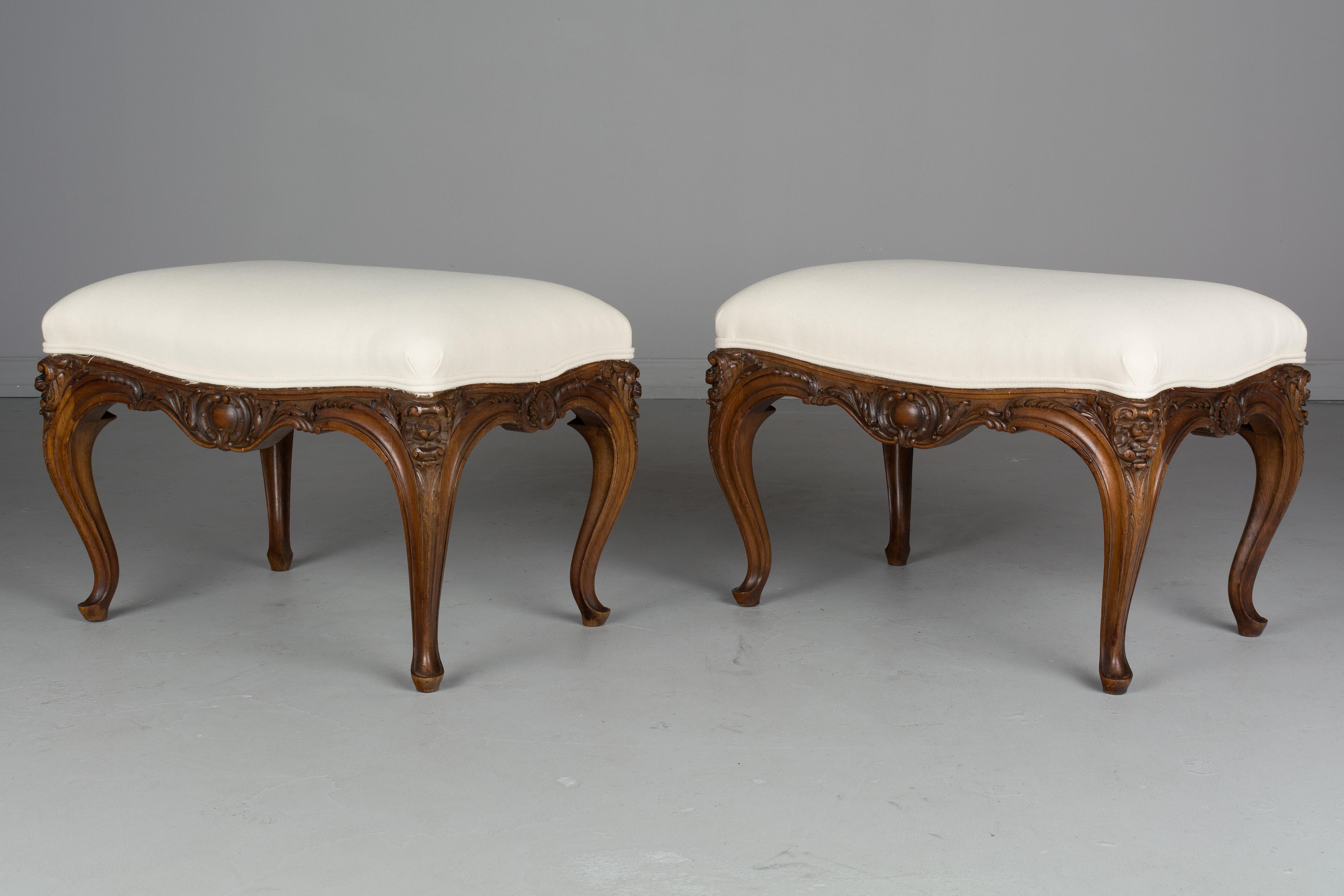 A pair of early 20th century French Louis XV style foot stools or benches made of walnut with nice carved floral details. Newly reupholstered. Please refer to photos for more details. We have a large selection of French antiques at Olivier Fleury,