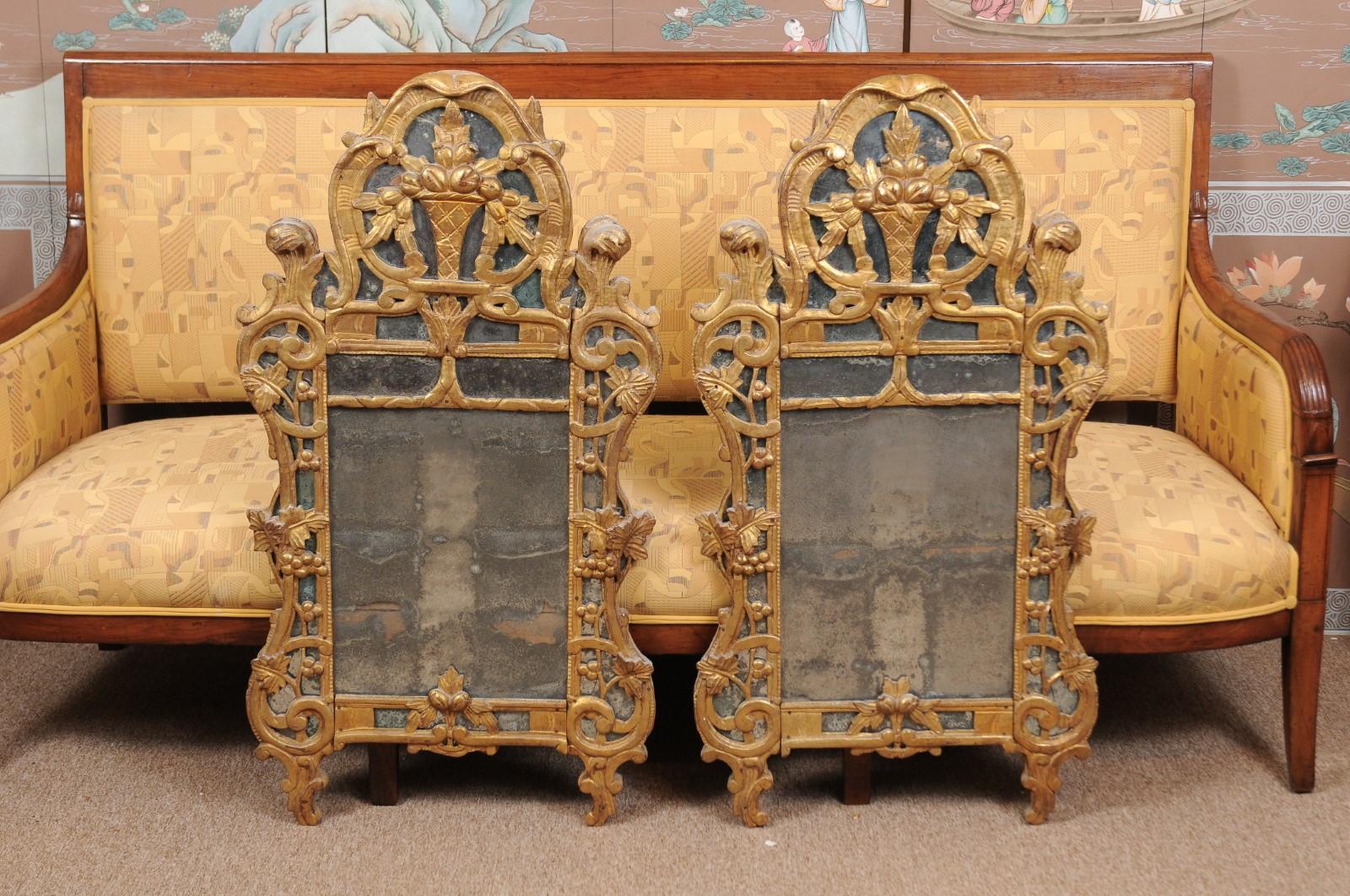 A pair of 19th century French Louis XV style giltwood mirrors featuring carved fruit baskets, grapevines and foliate scrolls mounted to mirror plates. The mirrors with oak back boards.