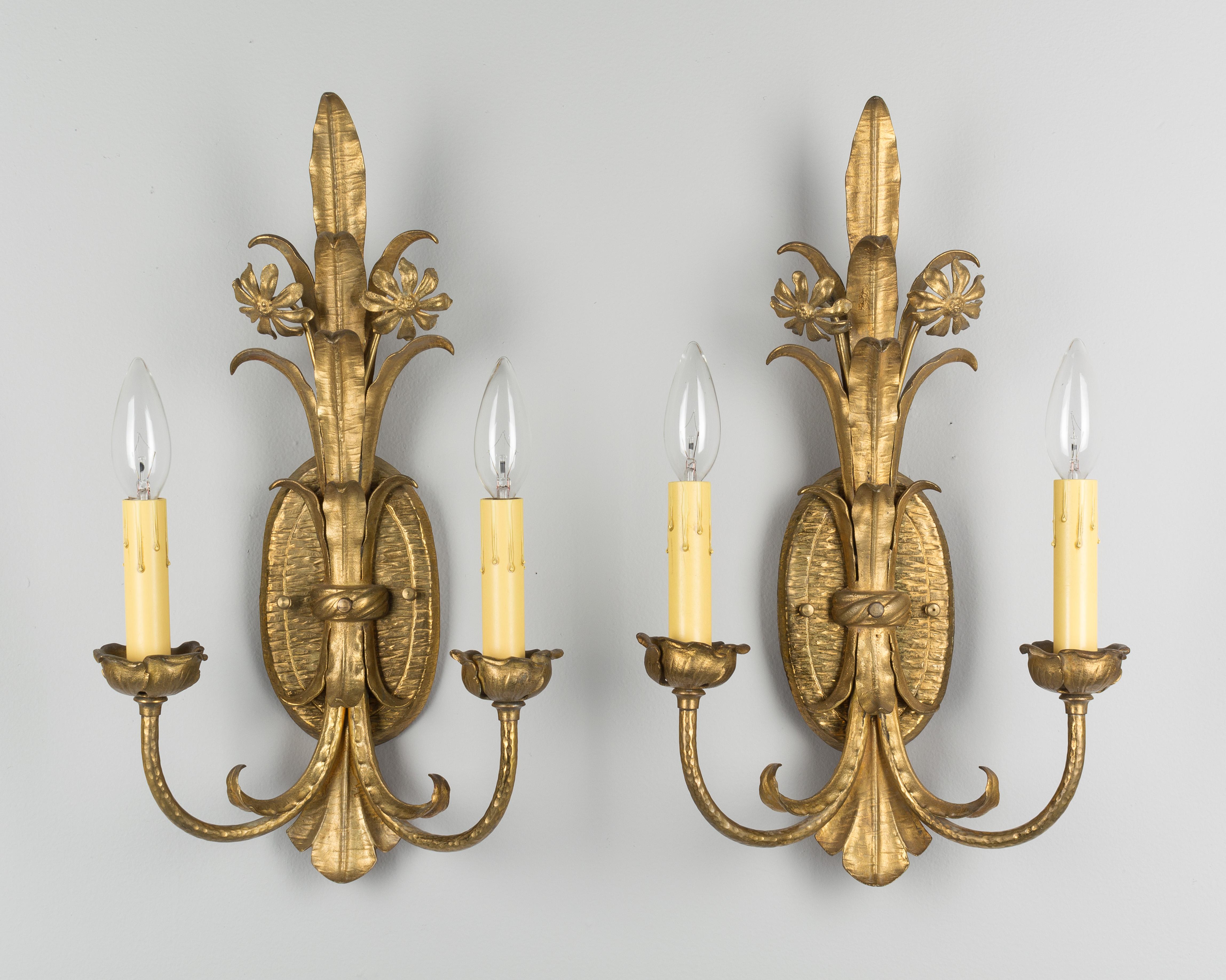 A pair of Louis XV style two-light bronze sconces. Oval backplate with foliate and floral motif. In excellent condition with bright gold patina. New candle covers. Wired as found.
 