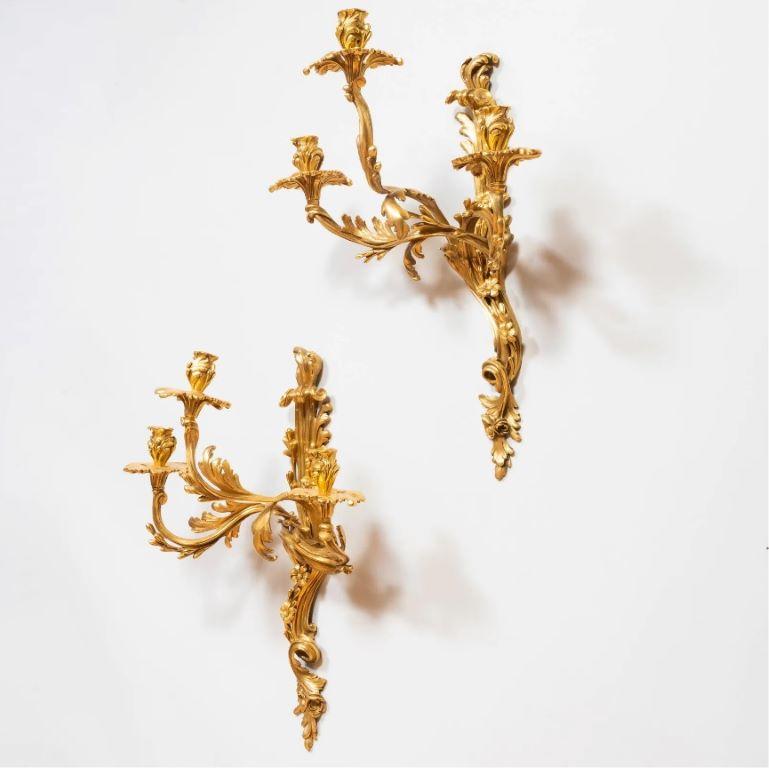 Pair of Louis XV style gilt-metal three-light sconces, 20th century. 

Minor wear and in good condition, probably re-gilt. Will need to be re-wired for use.