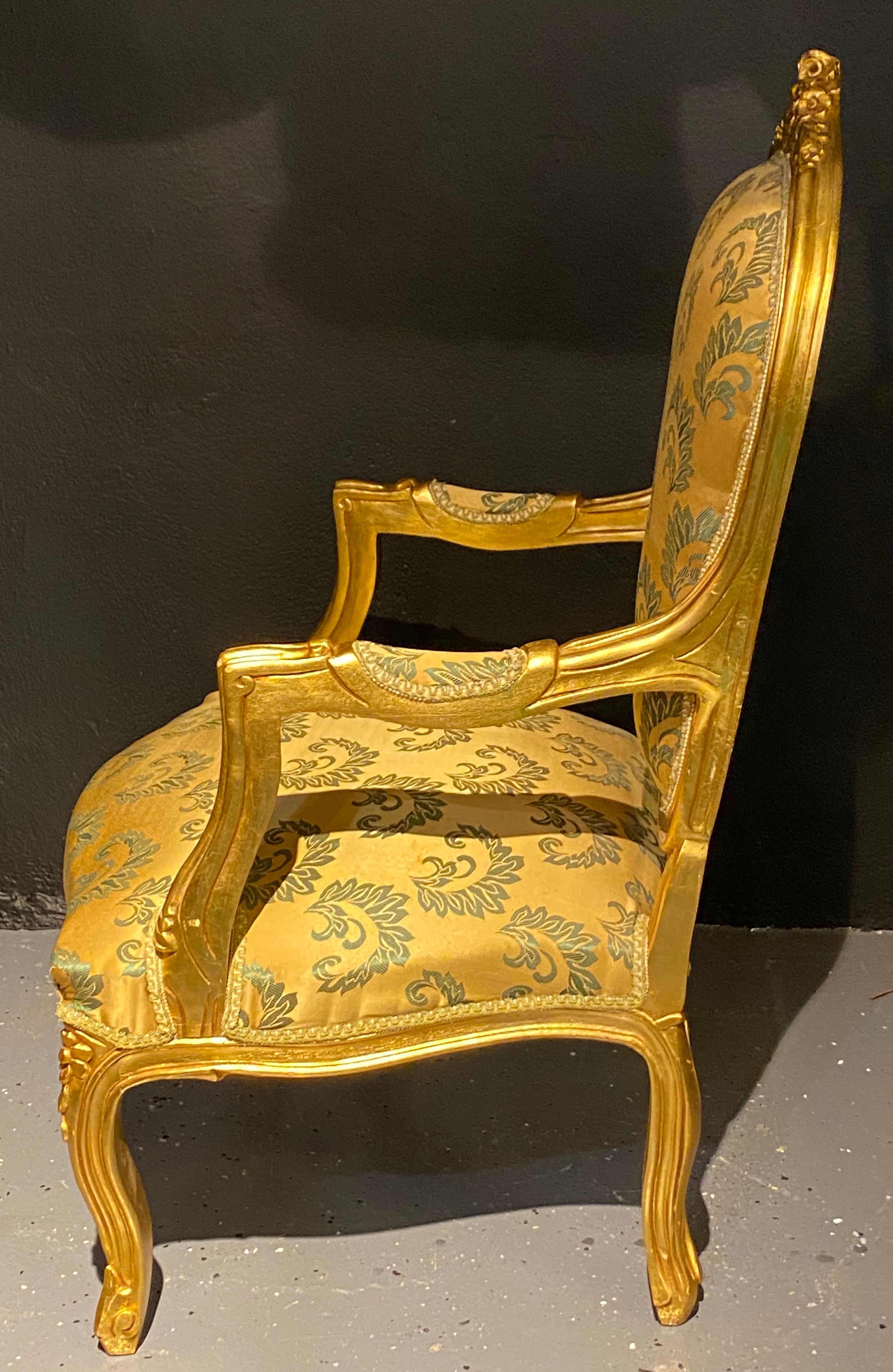 Pair of Louis XV style giltwood fauteuils or armchairs. This stunning pair of gilt gold Fauteuil chairs are covered in a satin Scalamandre upholstery reminiscent of the early French era of opulence. Each strong and sturdy frame having roses carved