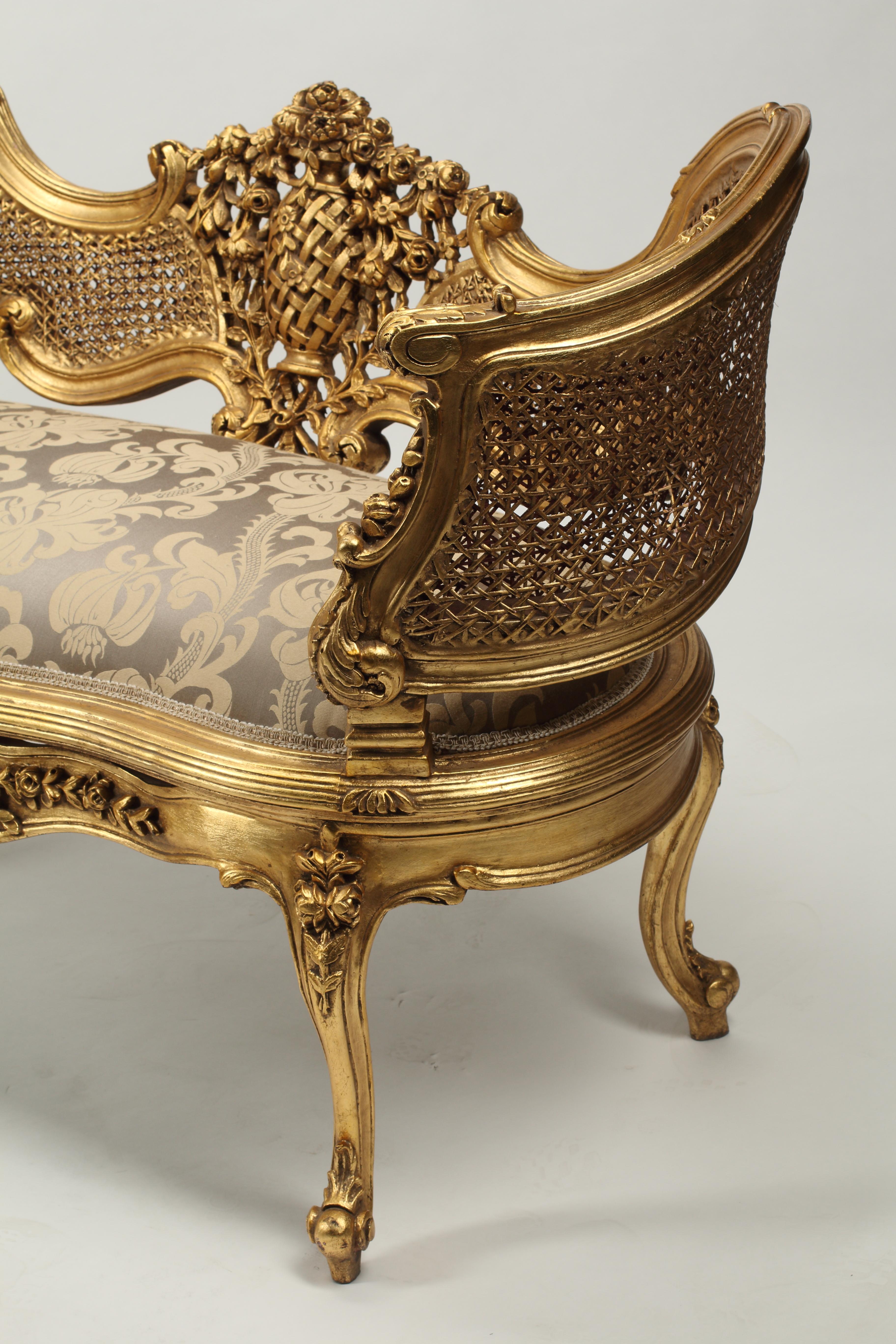 A lovely pair of giltwood Louis XV style upholstered settees. Caned seat backs and arms. Features highly decorative carvings of floral and foliage motifs on frame of settees. 
Newly upholstered with a taupe and golden fabric with simple braided