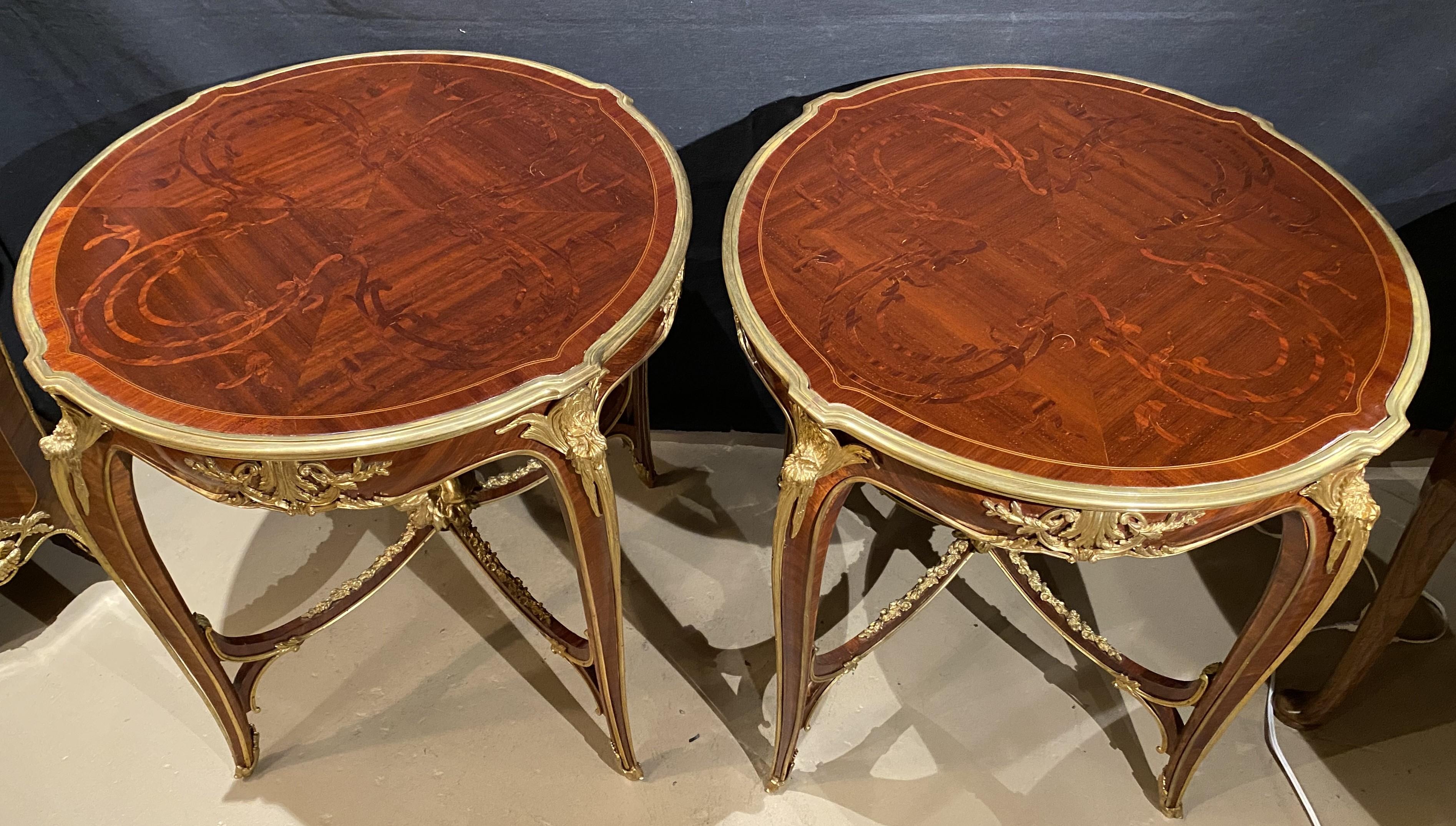An attractive pair of Louis XV style kingwood round center tables with subtle foliate marquetry inlay, and gilt bronze foliate mounts bordering the table top and frieze, all supported by cabriole legs with beautifully decorated medial stretchers