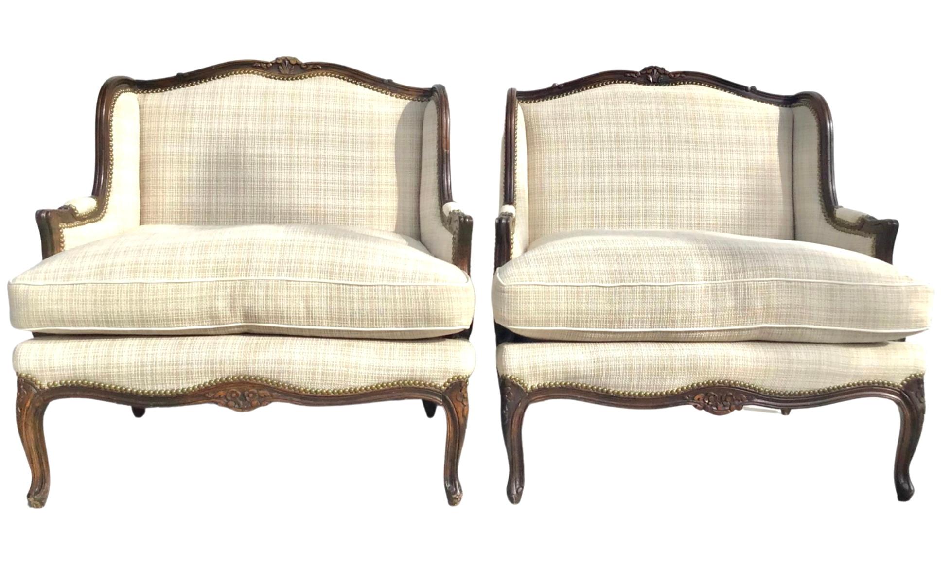 A pair of plush French Louis XV style Bergere or Marquis lounge chairs. The chairs are made of solid carved wood with the back and covered in a luxurious cotton fabric with brass nail heads. Sumptuous down cushions. Both cushions are removable. The