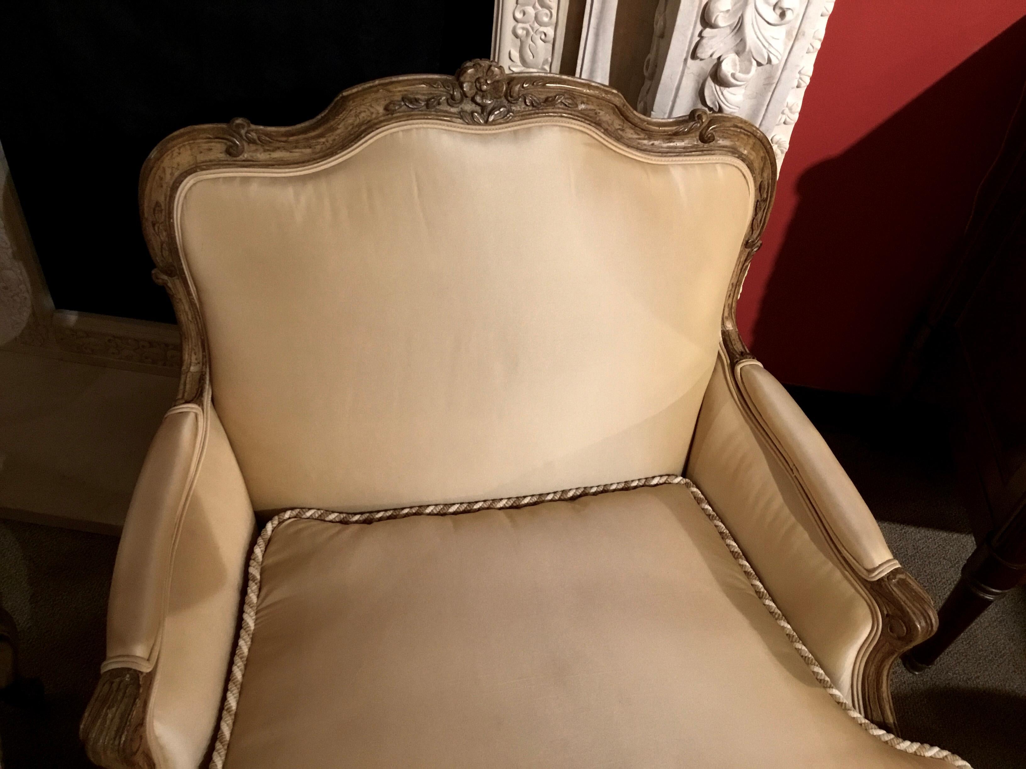 Handsome and comfortable pair of bergere Louis XV-Style chairs with floral and foliate 
Carving at the crest. Painted in creamy gold hue. The back is gracefully curved and extends
To a curved and nicely placed arm height. The bottom apron of these