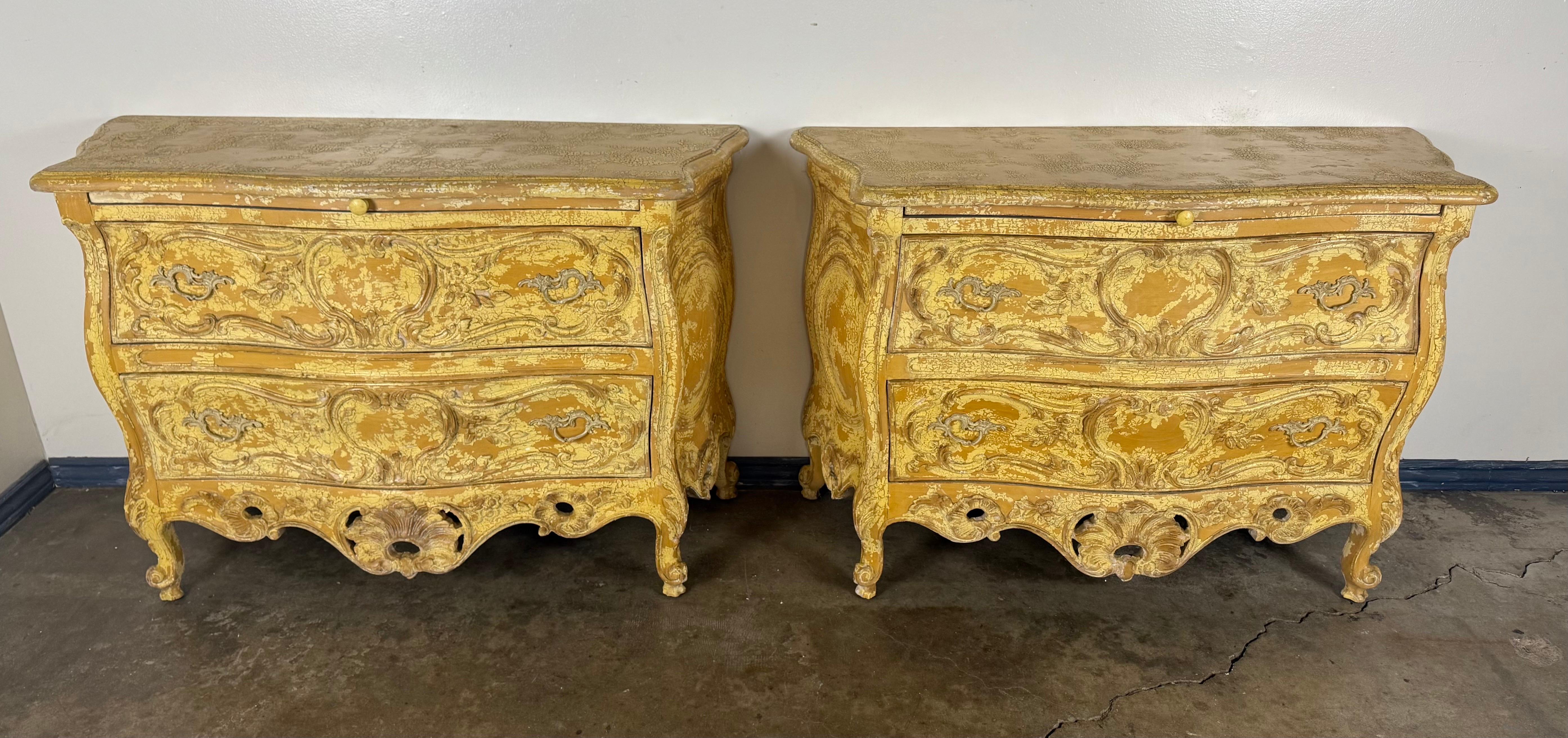 A wonderfully decorative pair of Louis XV–style bombe commodes, richly carved and finished in an exceptional timeworn painted surface. These chests feature the classic serpentine silhouette of the Rococo period—swelling fronts, dramatic curves, and