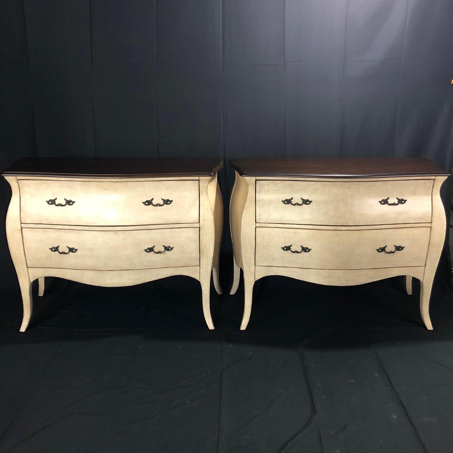 Beautiful pair of painted walnut commodes in the French Louis XV style having shaped stained walnut tops with lamb’s tongue molding and canted carved corners. There is brass aged hardware on the two drawers and the off-white paint treatment looks
