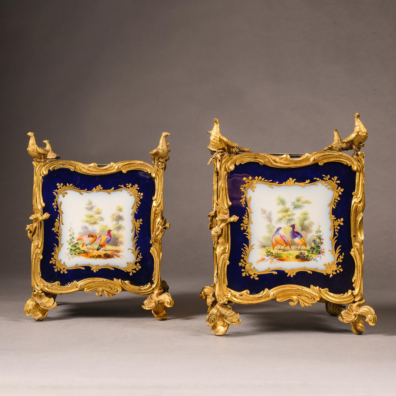This unusual pair of Sèvres-Style jardinières are each of square section inset with finely painted porcelain panels, depicting floral sprays and genre scenes in the manner of Boucher.  The gilt-bronze mounts are finely cast with scrolling rocaille