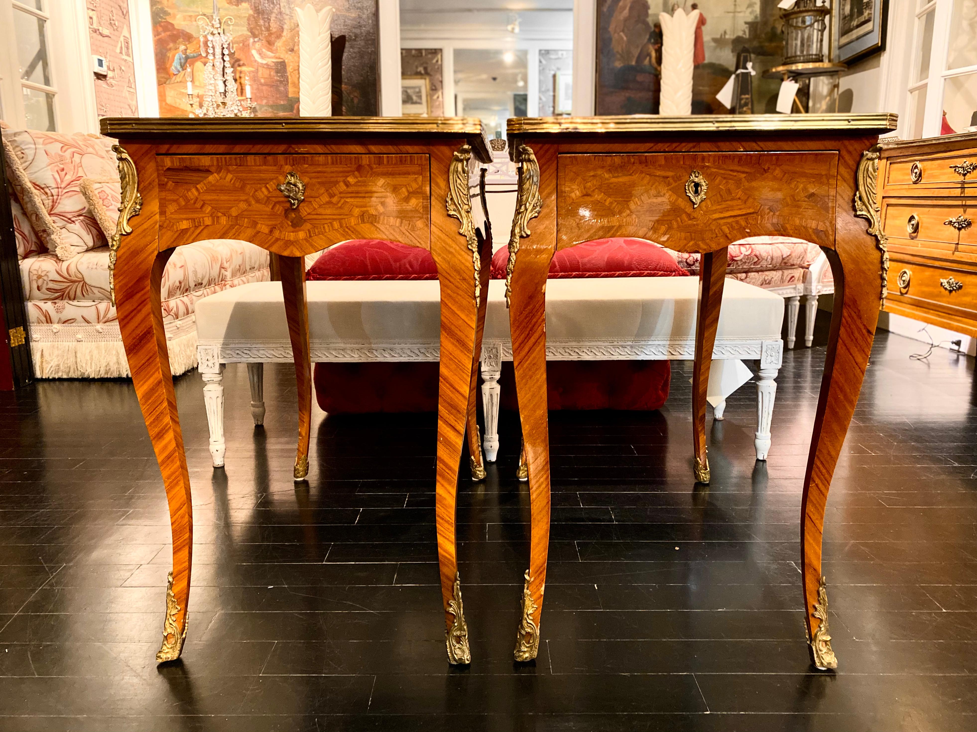 Pair of Louis XV style end or side tables. Each has a long drawer opening from the side, with gilt bronze sabot feet, bronze detailing around the top and along the legs, and keyhole detailing. Marquetry finish with lovely golden tones. Multiple