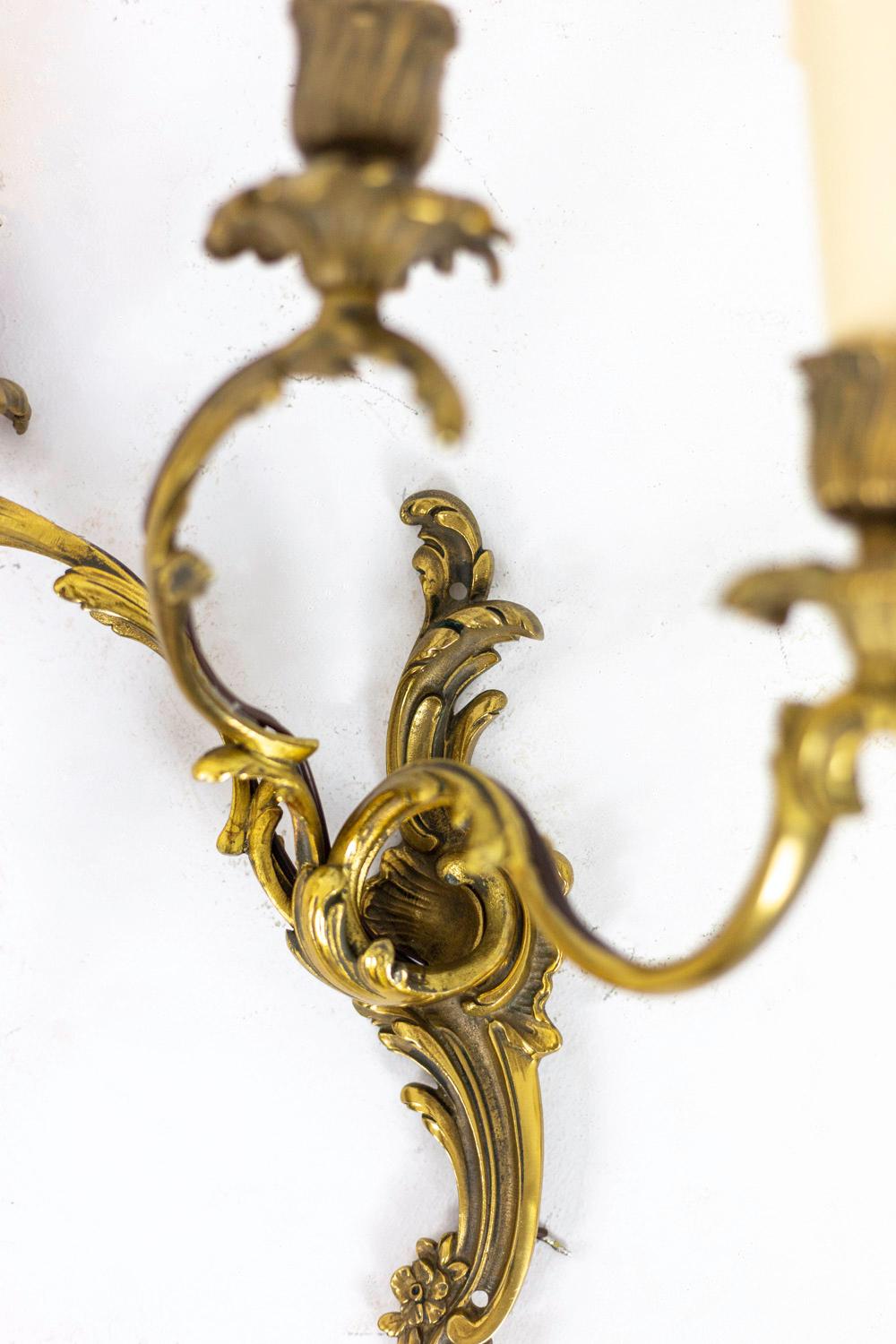 Pair of Louis XV style wall sconces in gilt bronze with three fires. Agrafe decor on which are fixed three scroll shape branches. Cups and bobeches decorated with acanthus leaves.

Work realized in the 1950s.

New and functional electrical