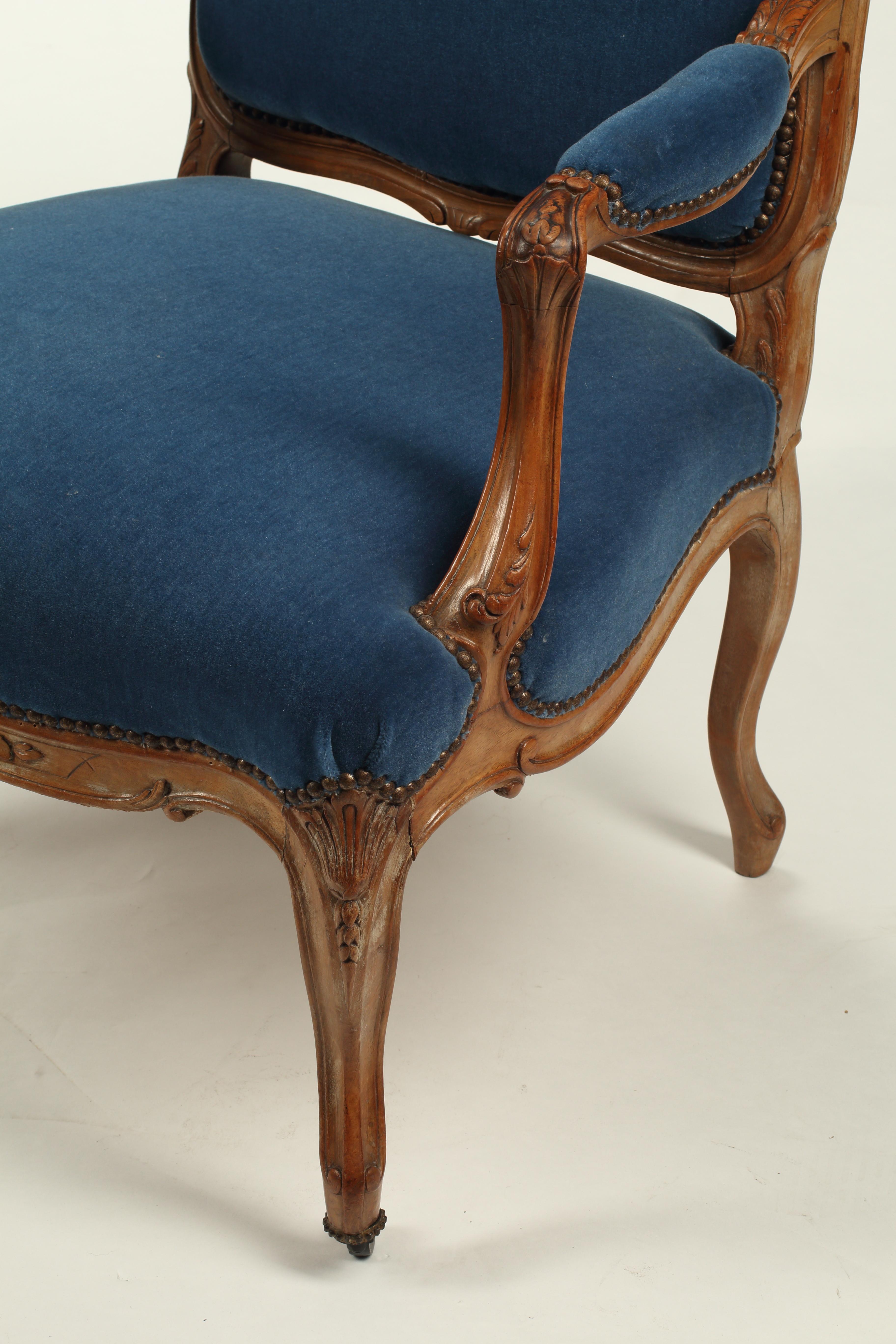 Cette paire exquise de fauteuils de style Louis XV rehaussera n'importe quel espace de vie. Le noyer, sculpté à la main, présente des motifs feuillagés et des volutes sur la couronne du dossier, les épaules, les accoudoirs et la frise. Les lignes