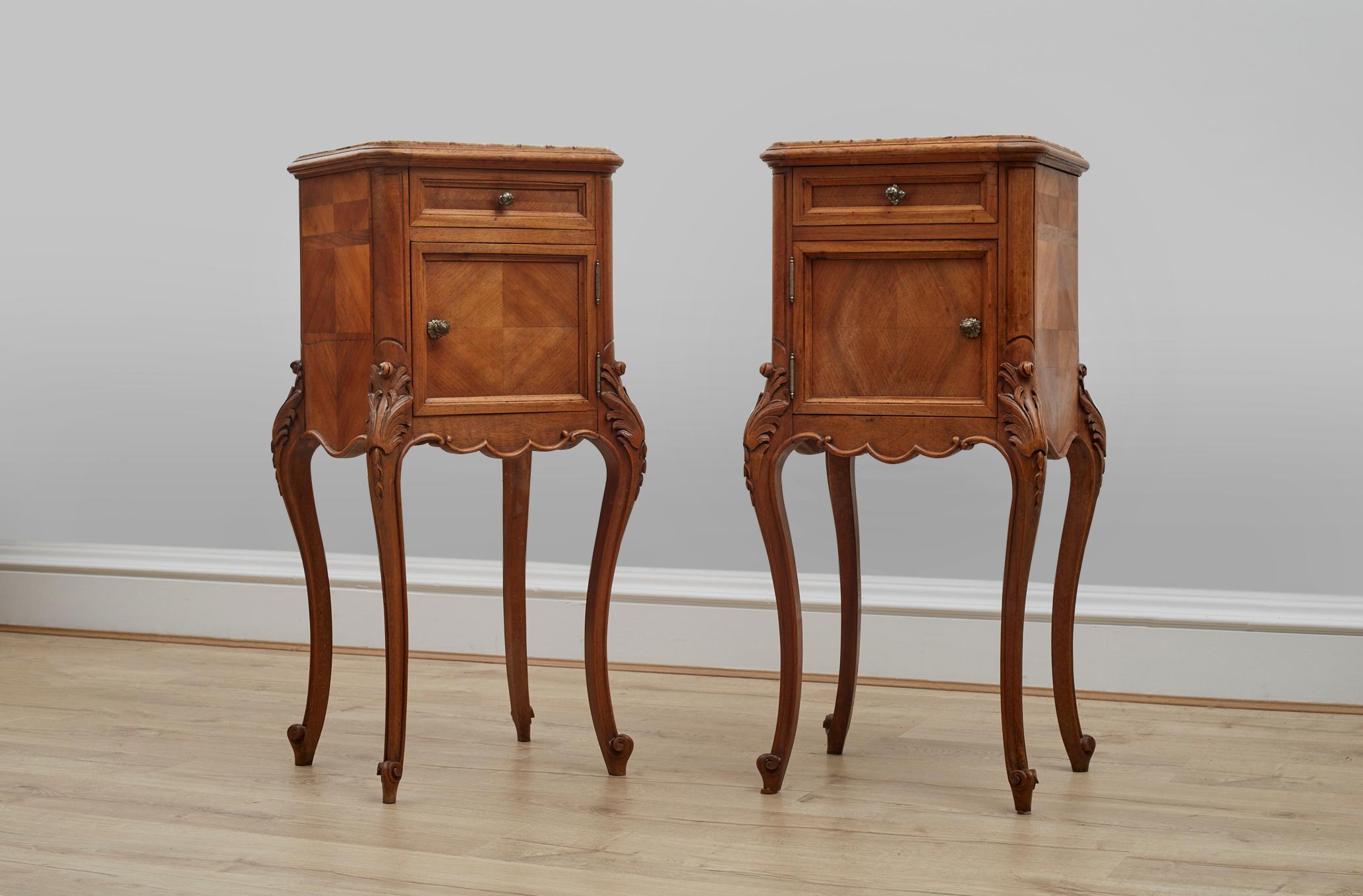 Pair of  circa 1920's Louis XV Style walnut marble topped side cupboards. 

These matching pair of elegant side tables feature a storage compartment below a drawer with beautiful brass handles.
