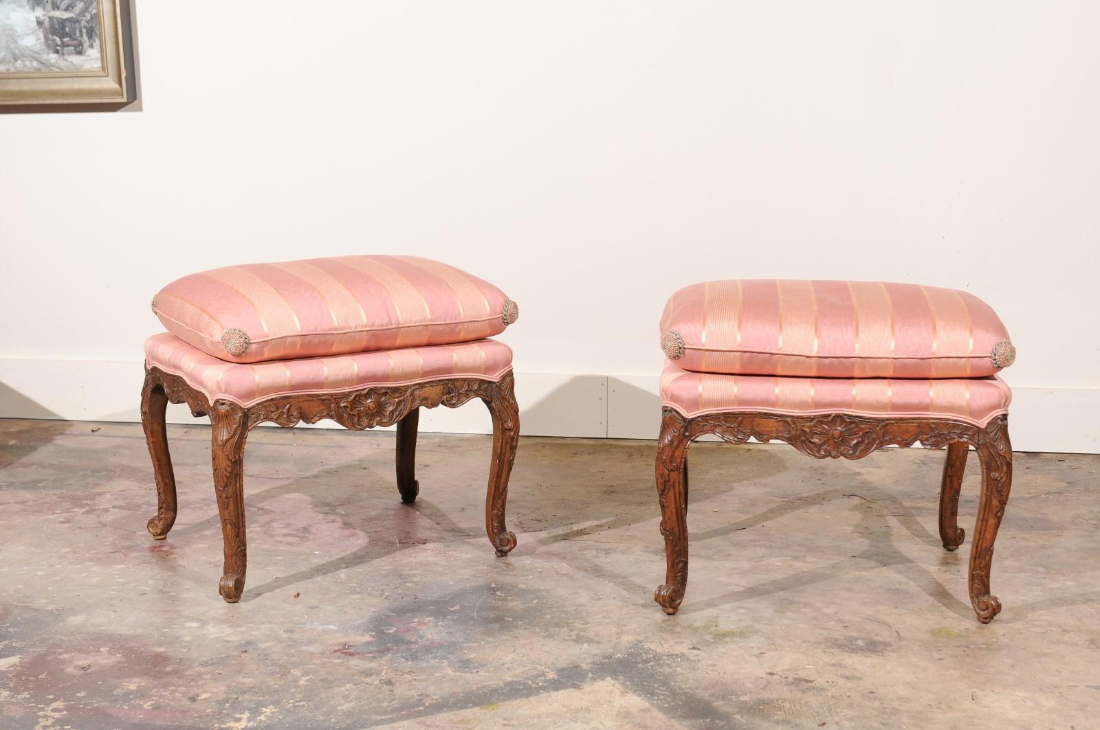 This stunning pair of Louis XV stools stands on four beautifully carved cabriole legs and scalloped apron. The seat is upholstered in a stripe fabric in two shades of salmon /coral topped with a cushion in the same fabric. A rosette on the four