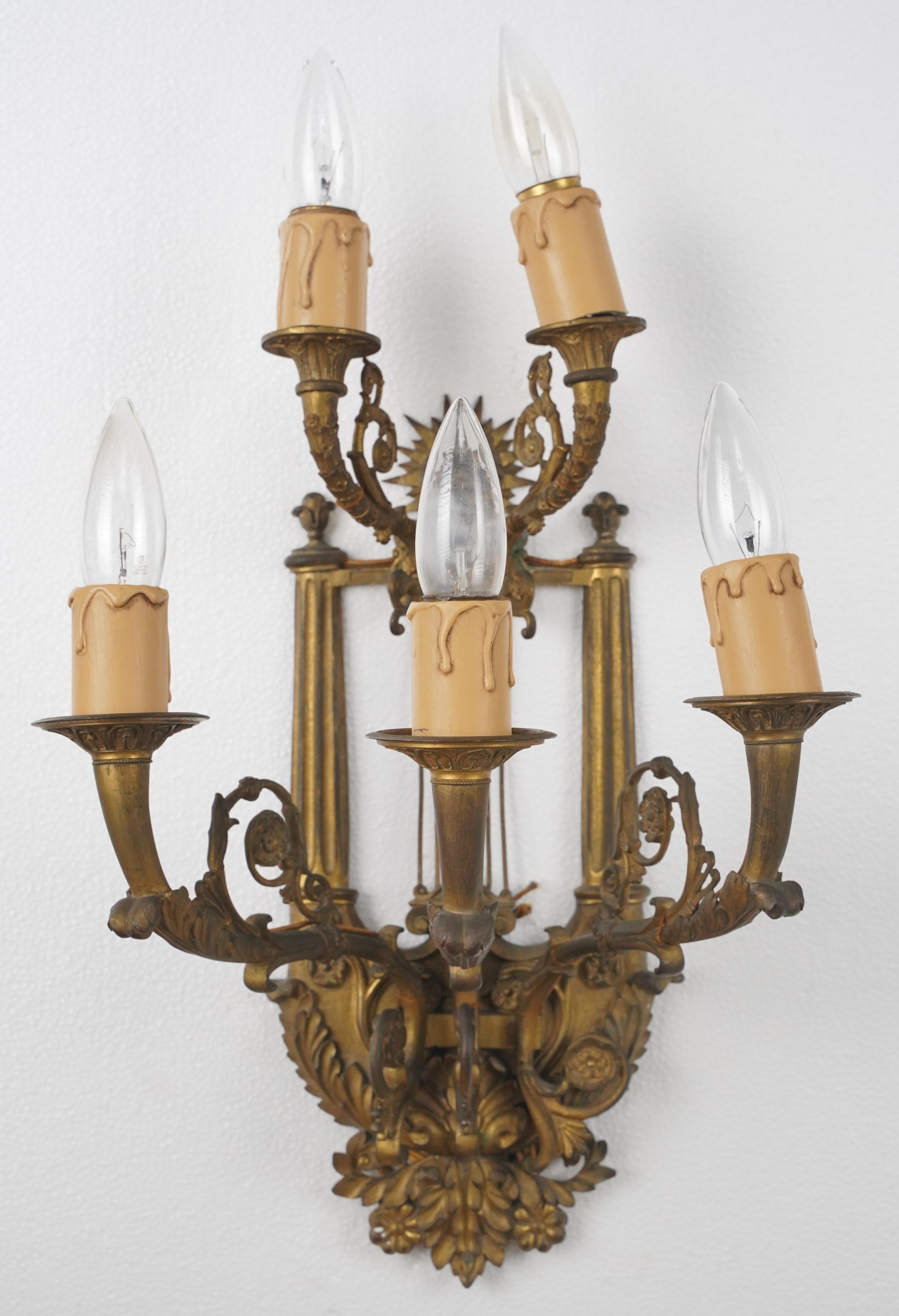 19th Century Louis XVI style wall sconces featuring figural putti, acanthus leaves, urns, and floral motifs. Both sconces are made of bronze with an aged patina finish. Each sconce requires five Edison style candelabra light bulbs. Cleaned and