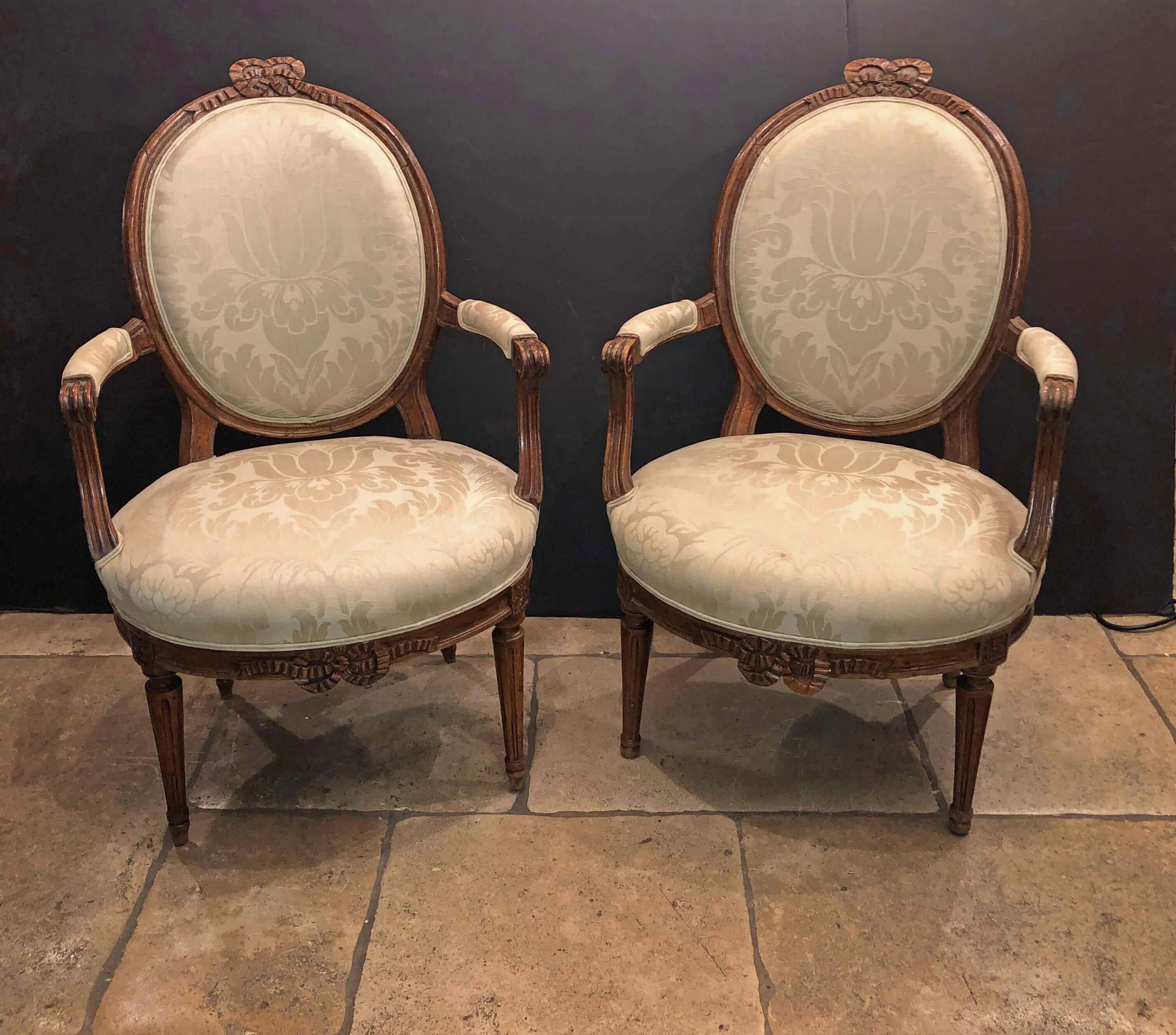A matched pair of French Louis XVI carved walnut oval back Fatueil a La Reine with oval seats, carved bowknots, 20 fluted arms and turned, tapered and fluted legs.