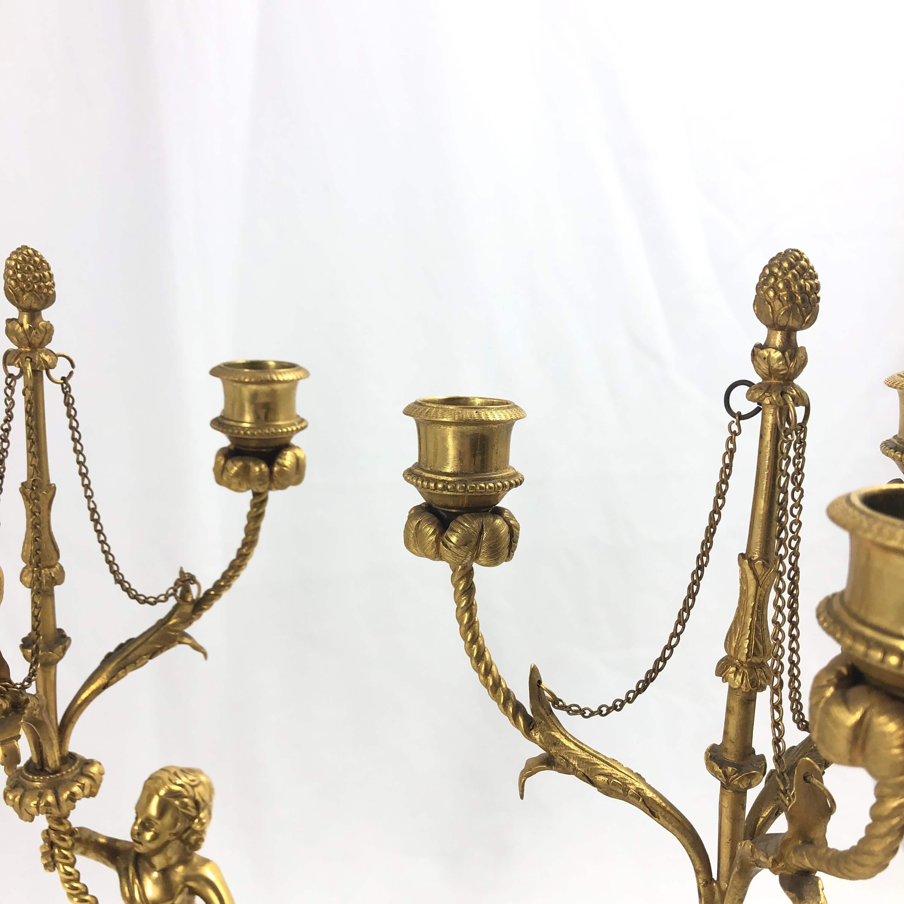 A fine pair of French Louis XVI gilt bronze putti candelabra with each putti holding a three-light arm with floral motifs, acorn finials, and raised on a marble pedestal base with a bronze wreath mount.
