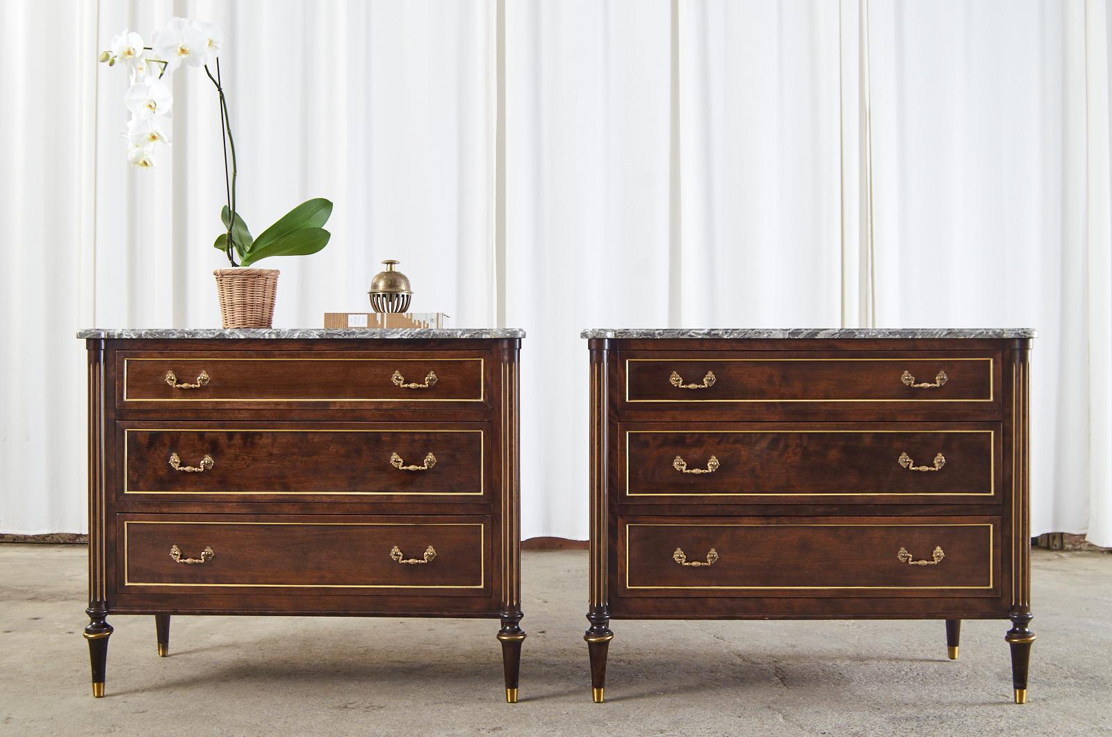 Opulent pair of French mahogany commodes or chest of drawers featuring dramatic variegated marble tops. The cases are crafted in the grand Louis XVI taste from radiant mahogany having bronze mounted borders on the three storage drawers and side