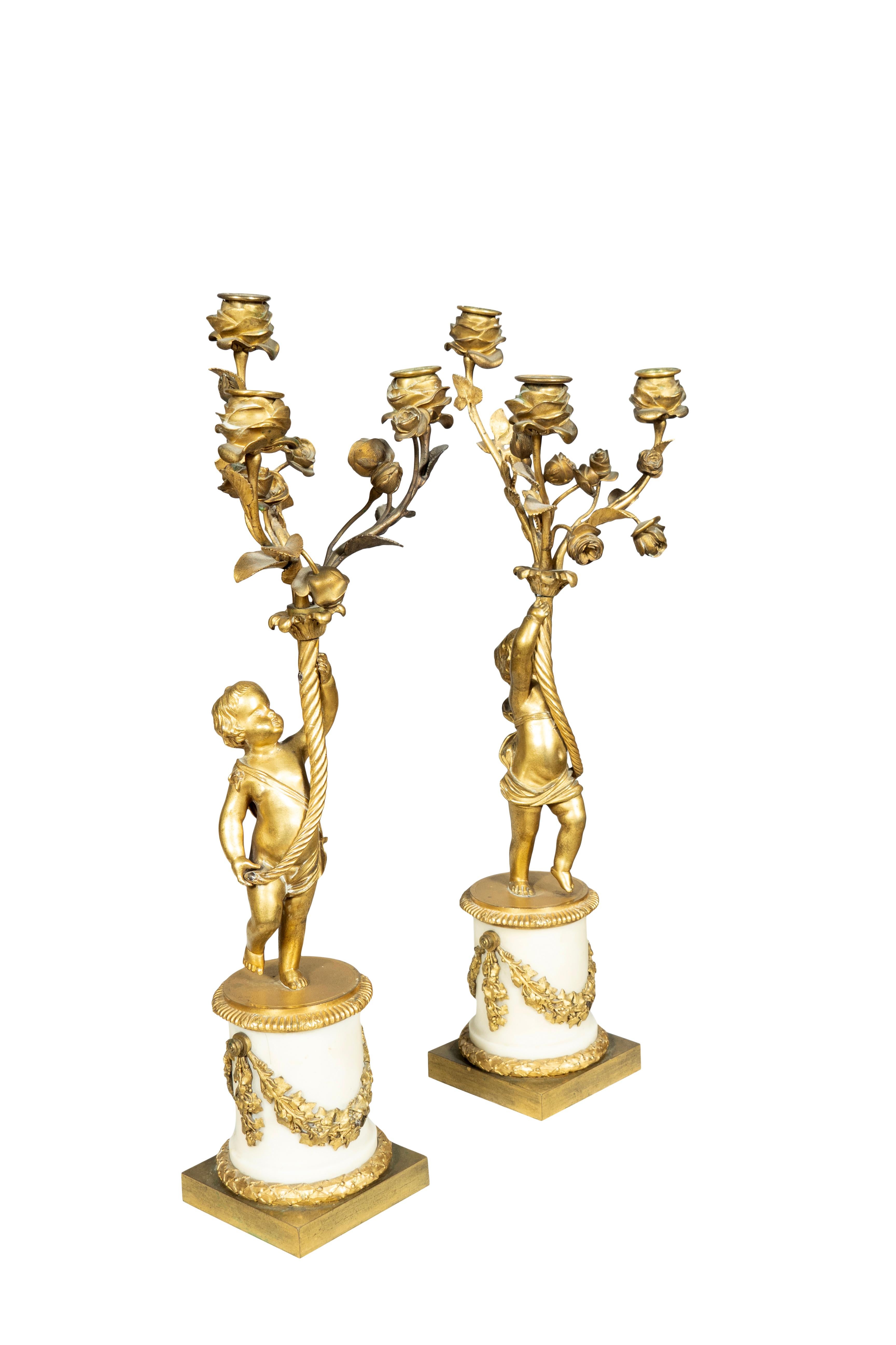 Cherubini che sorreggono un candelabro a tre bracci con rami di rosa e portacandele a forma di fiore. Rondine in bronzo dorato montata su una base circolare in marmo bianco. Basamento quadrato in bronzo.