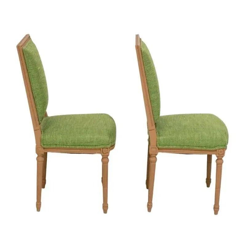 A pair of Louis XVI painted side chairs with green fabric upholstery.  The square back pair of chairs have a neutral painted frame and straight, reeded, round legs with a carved floral decoration inside a square at the top of each leg.  The apple
